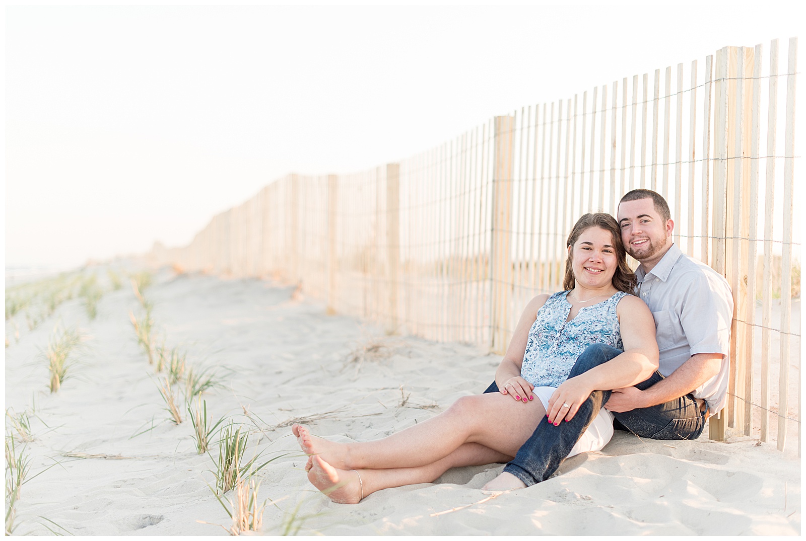 couple sitting on beach leaning against fence