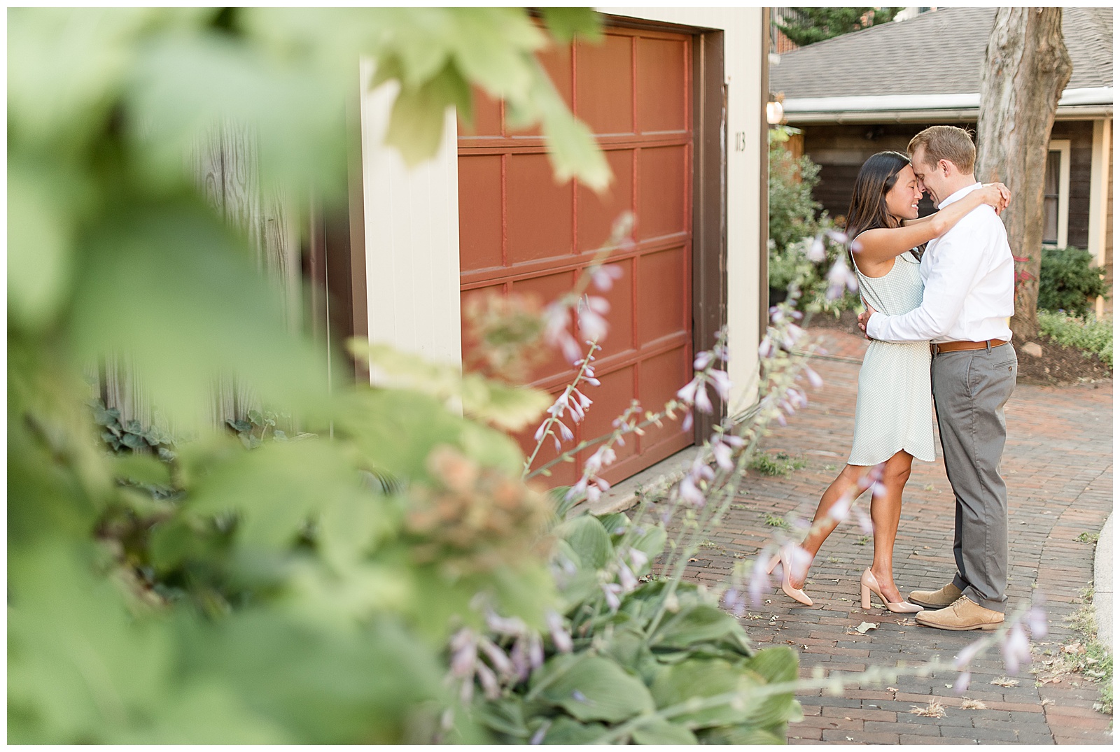 couple forehead to forehead and girls arms wrapped around his neck as the photo is taking through a floral bush