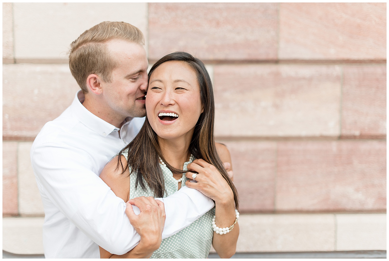 girl laughing off left of camera as guy gives her kisses on her check with arms wrapped around her 