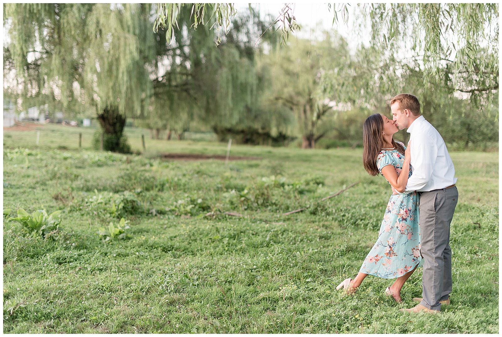 girl dipping back as guy leans in for kiss in front of willow trees