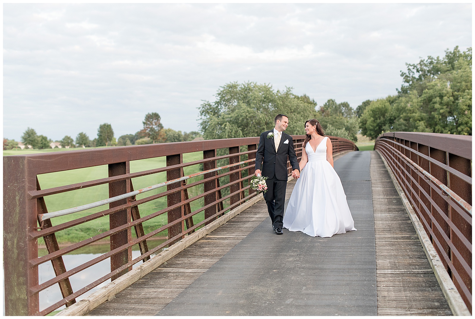 couple walking hand in hand, looking at each other across bridge at golf course
