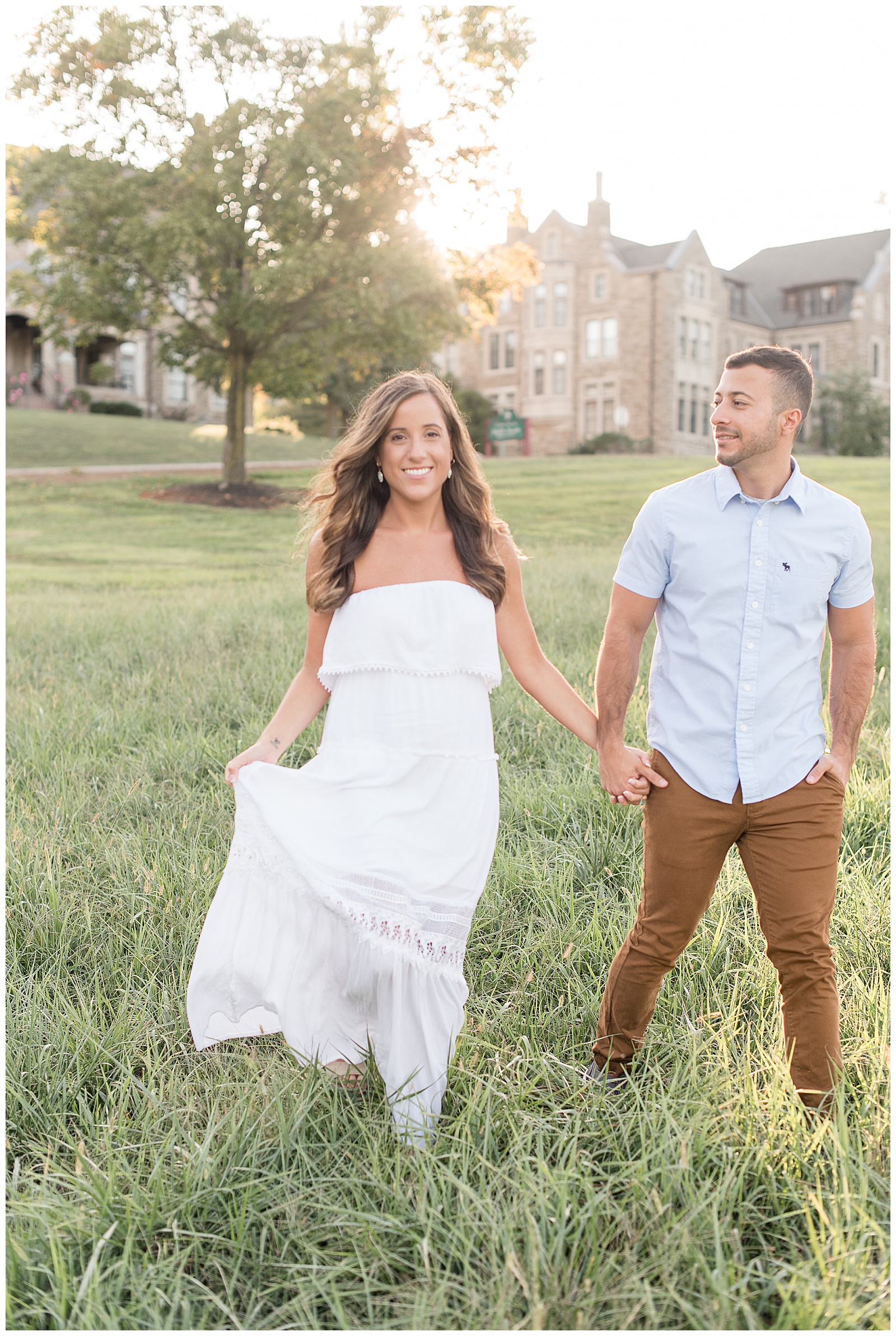 couple walking in open field of grass, as she smiles at the camera
