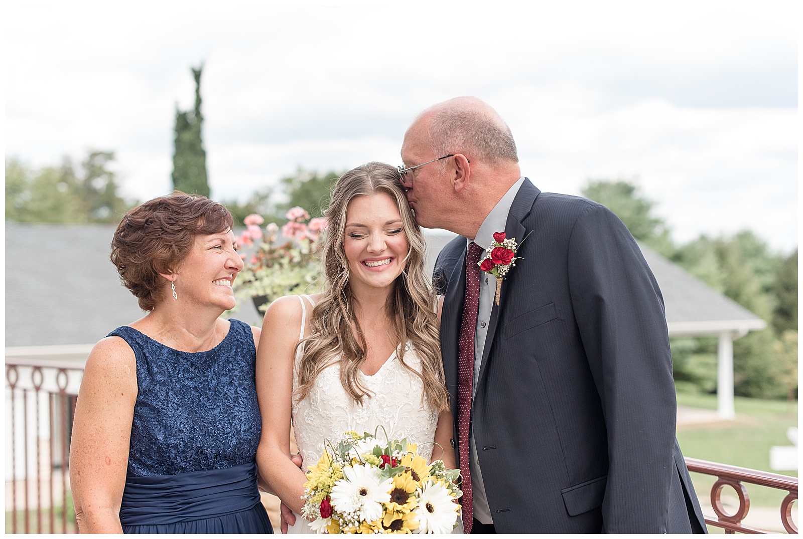 bride photo with her parents and dad is kissing her on the head