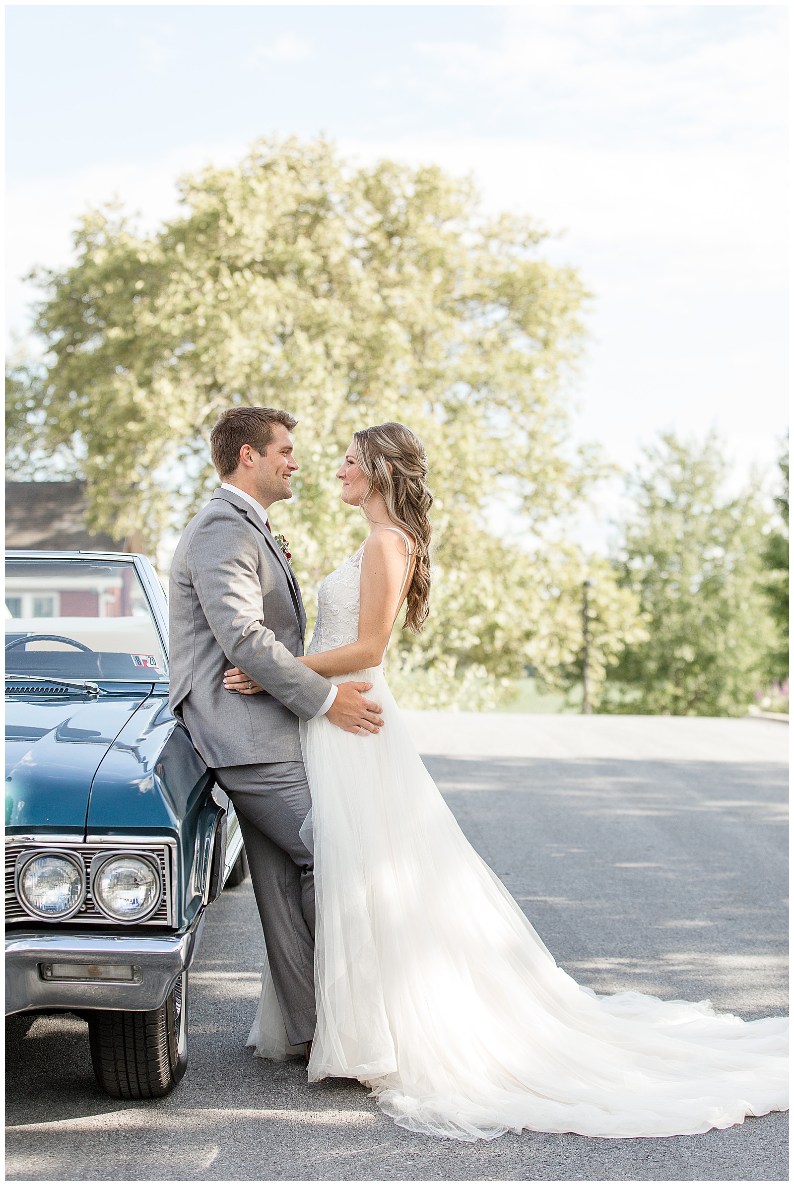 groom leaning against old buick with bride leaning against him