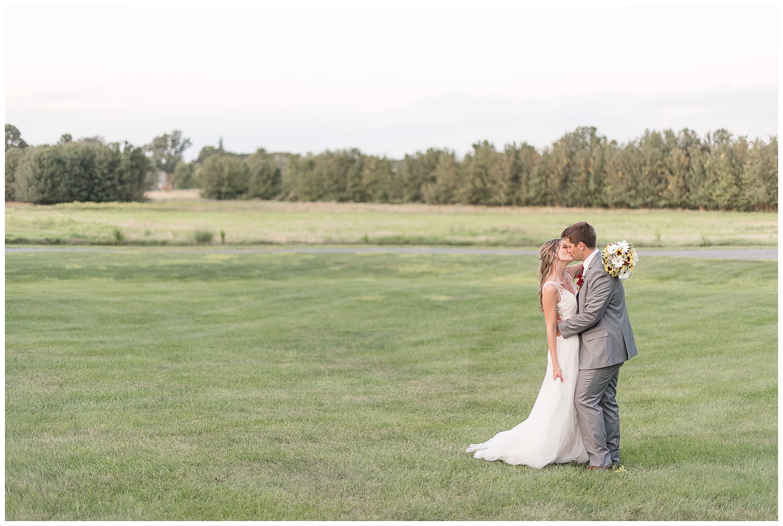 husband and wife kissing in open grass field