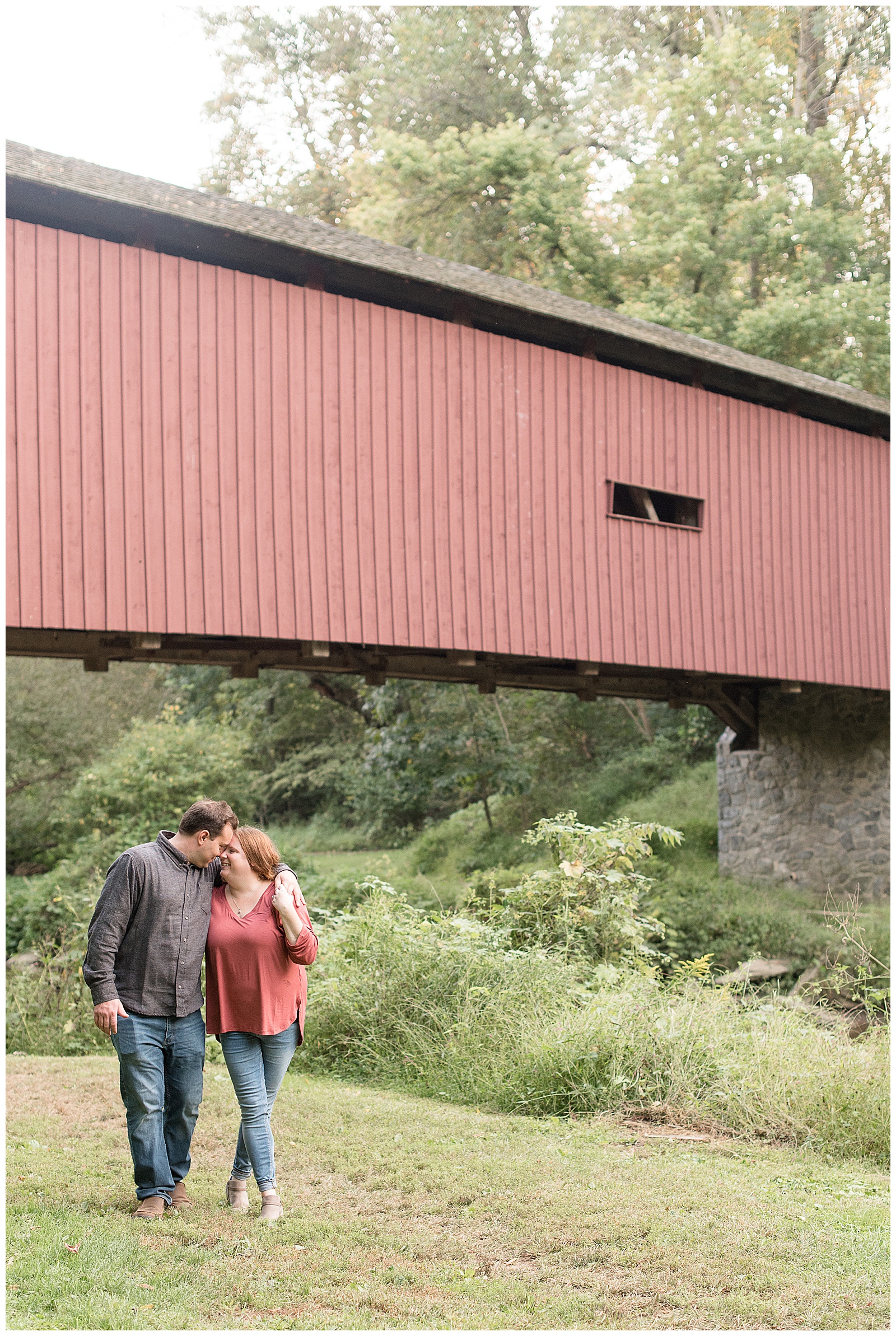couple walking towards camera looking at each other in front of covered bridge