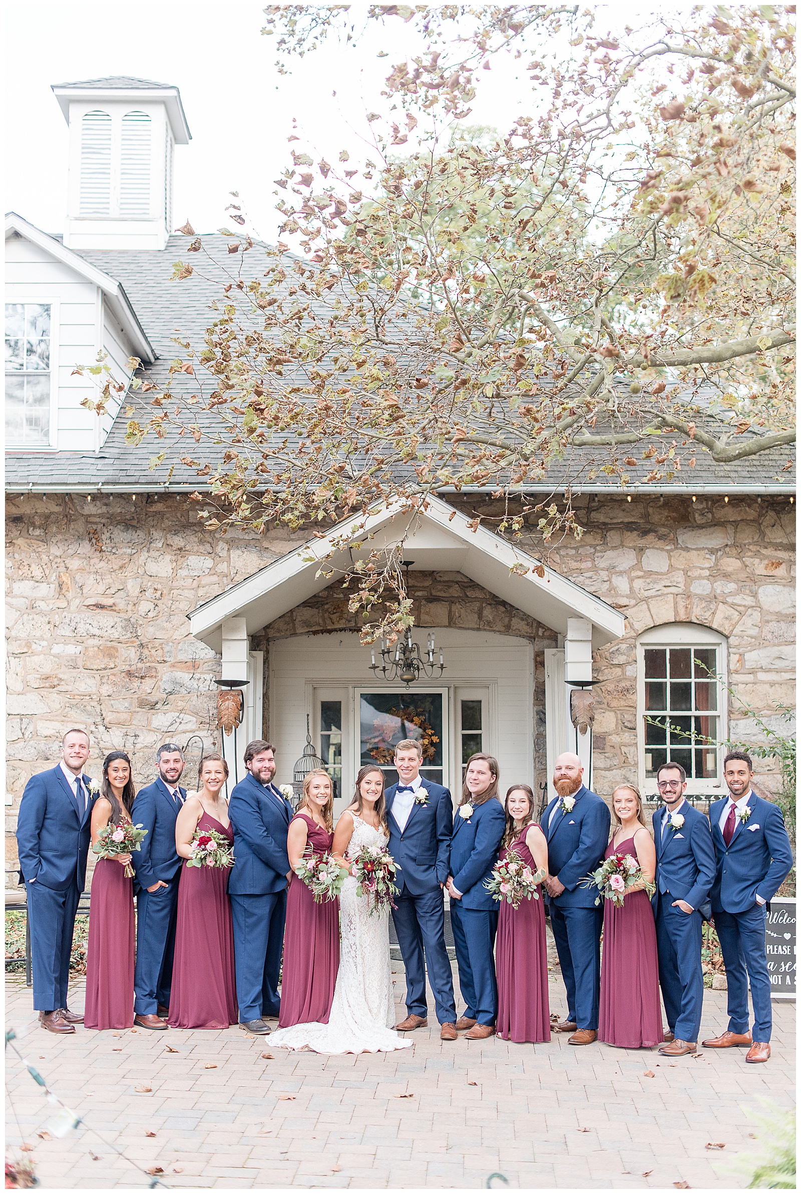 full bridal party smiling in front of stone house