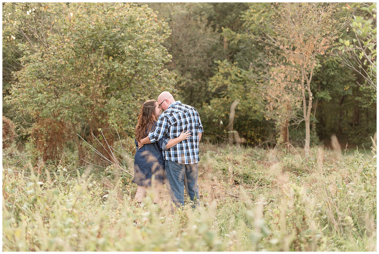 couple facing away from camera and touching foreheads in a field of wild grass