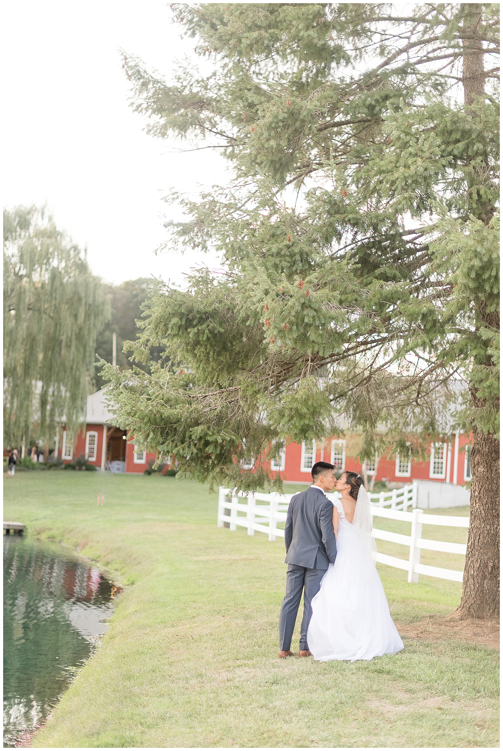 husband and wife kissing with venue behind at Pond View Farms