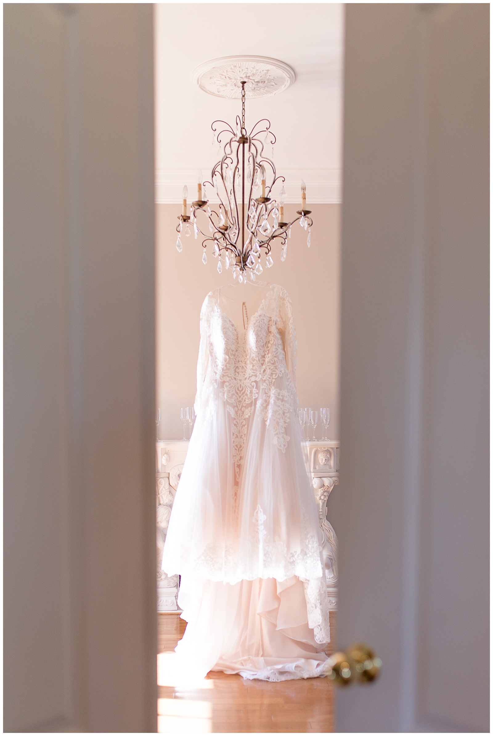 wedding dress hanging off chandelier with camera peeking through doors