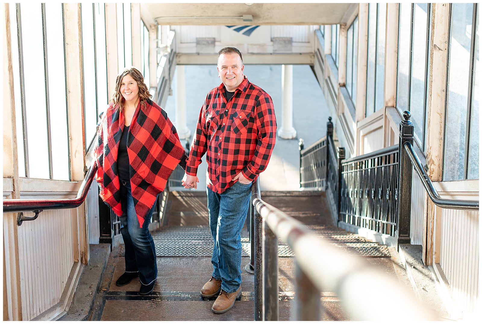 couple standing in stairwell going down to train tracks smiling at camera