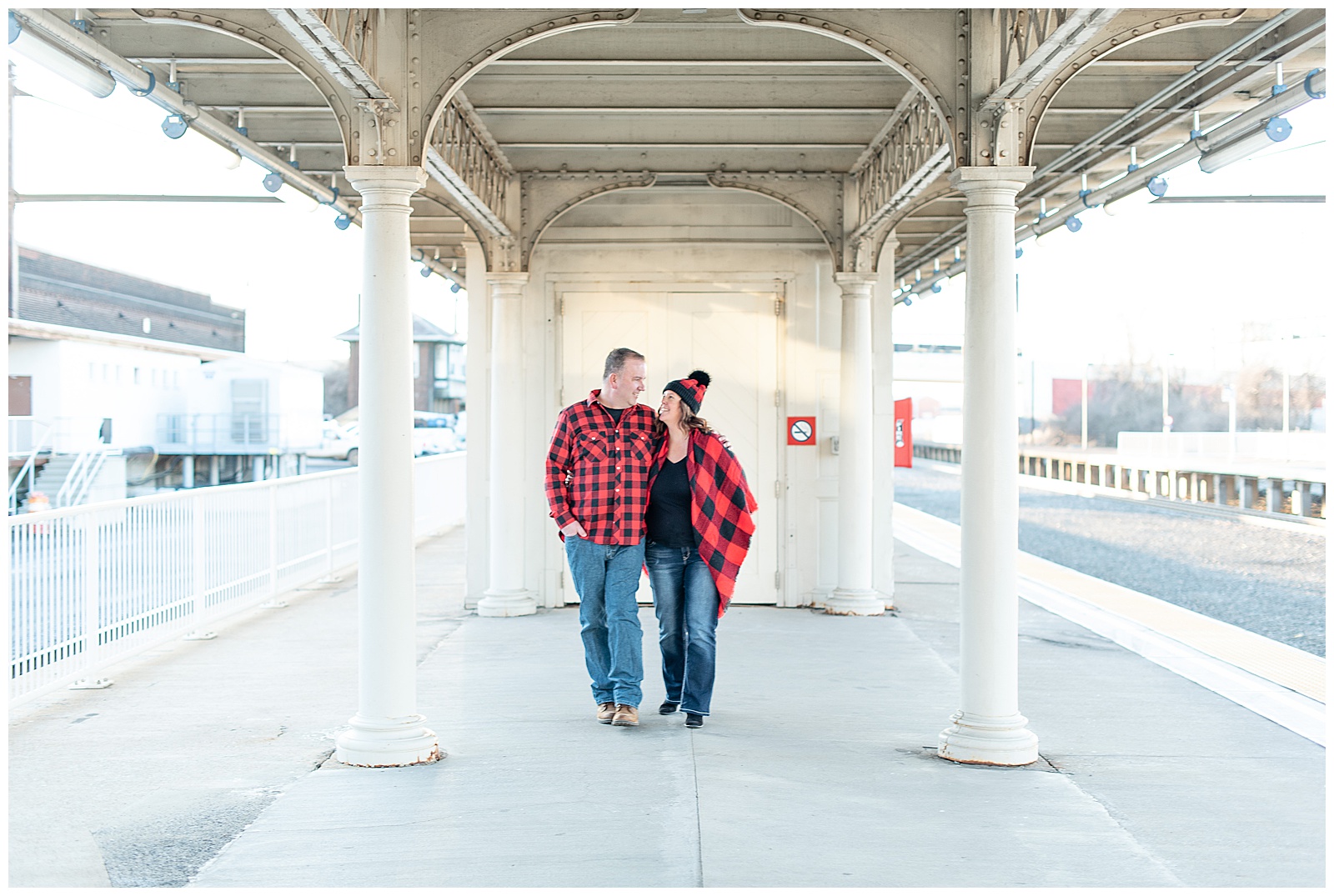 couple walking with arms wrapped around each other down beside train tracks