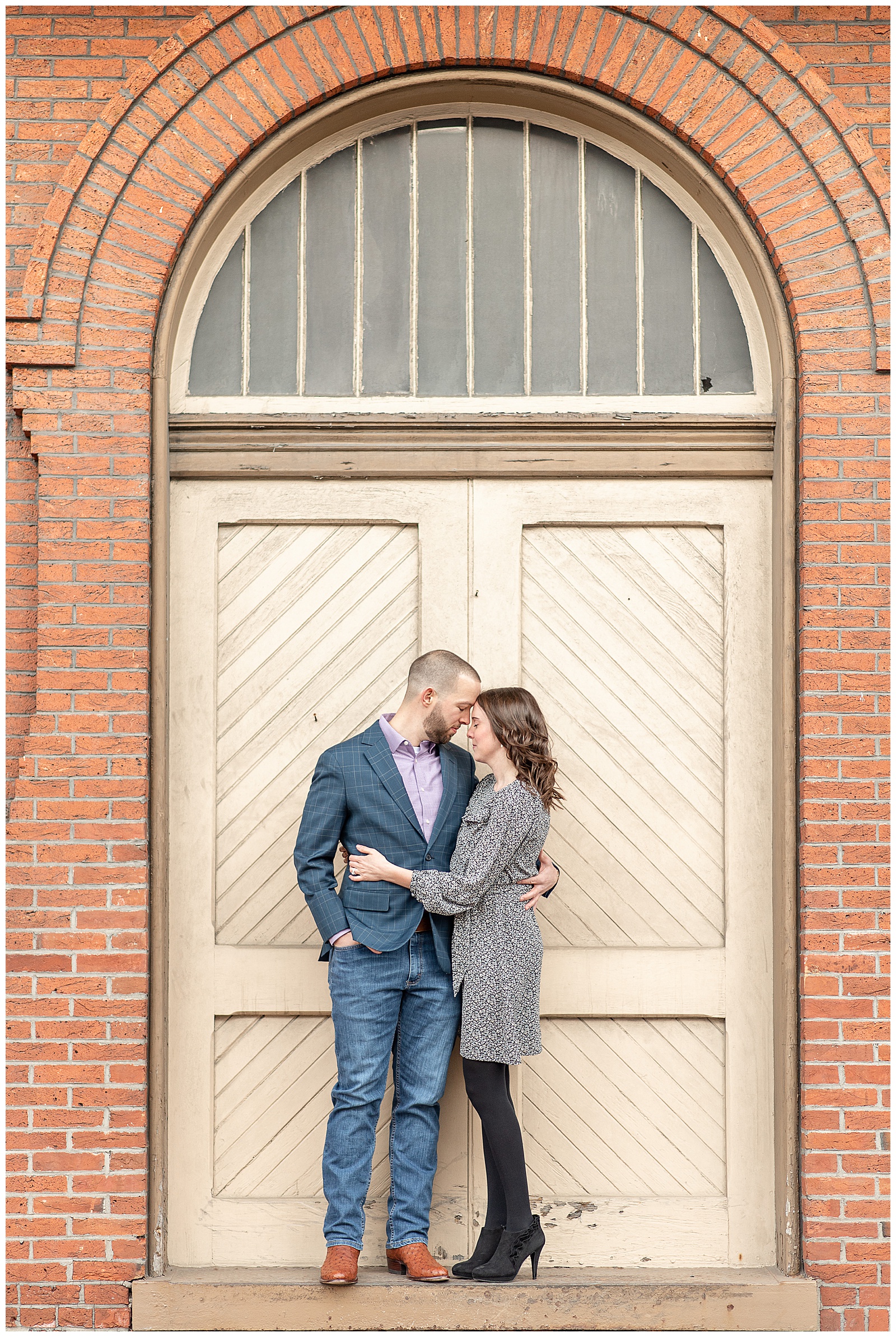 couple resting heads together in front of light yellow arched door