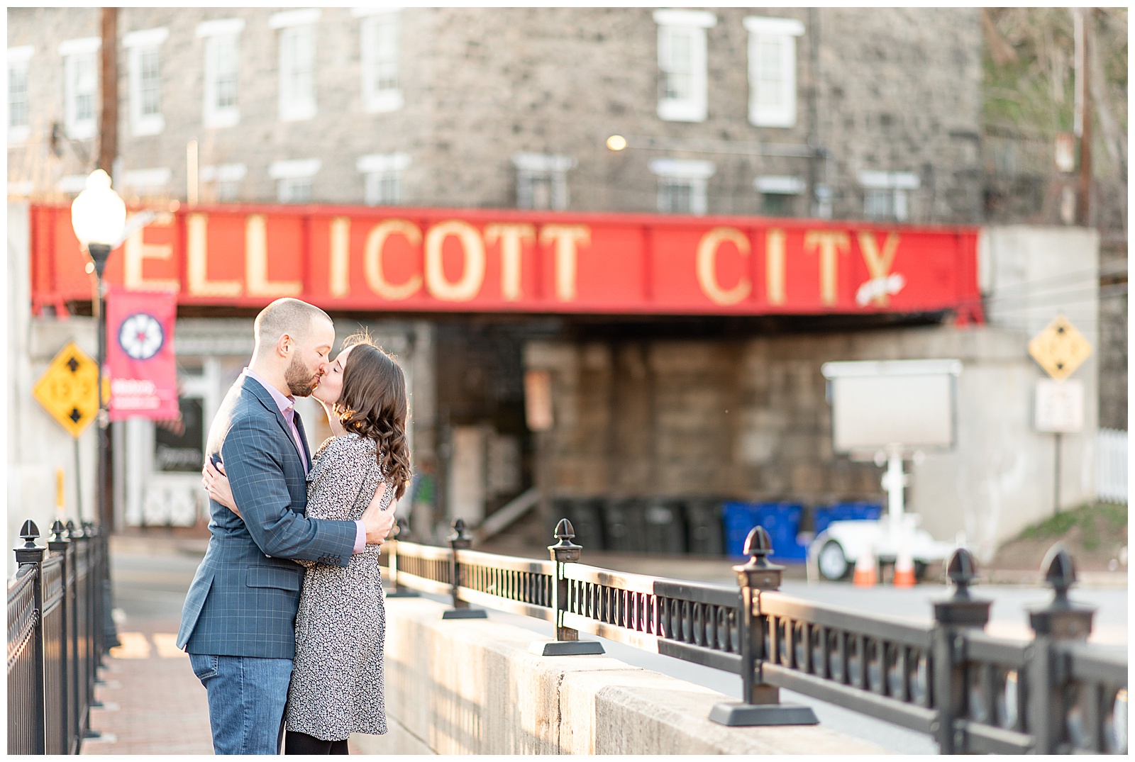 couple kissing on bridge with Ellicott City sign behind them