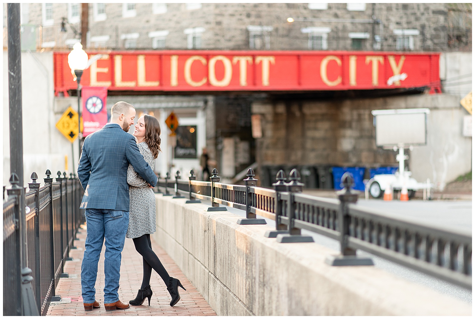 couple sharing a kiss on a bridge with Ellicott City sign behind them