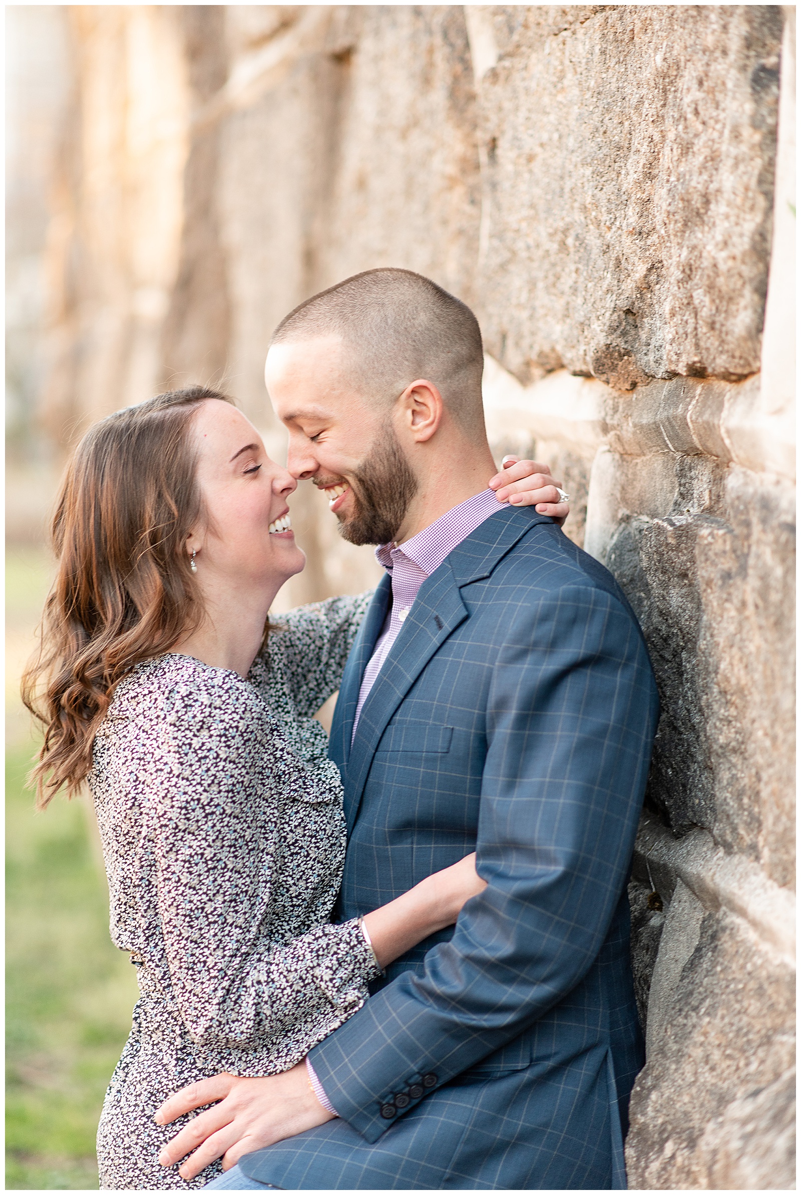 couple leaning against stone wall and touching noses and laughing
