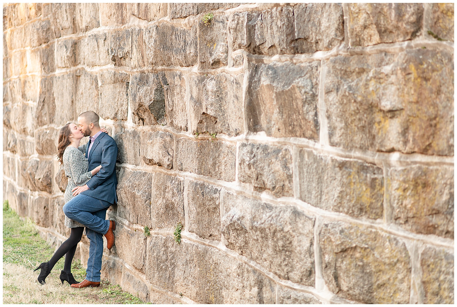 couple sharing a kiss against a stone wall