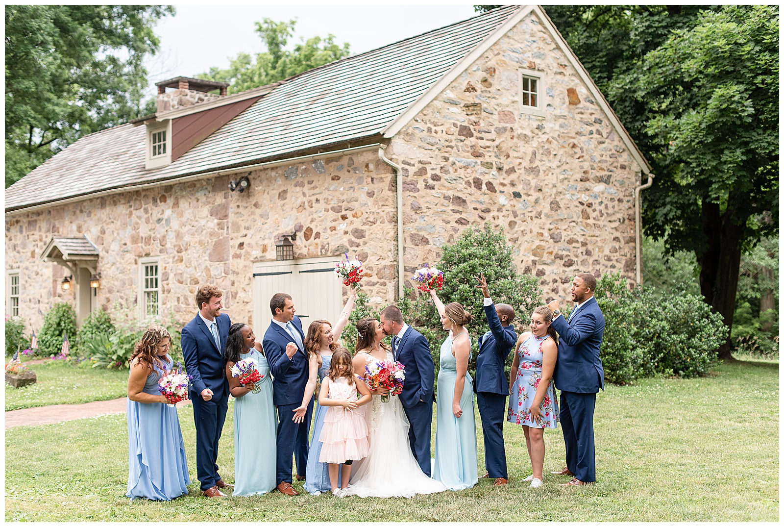 full bridal party cheering and bride and groom kissing