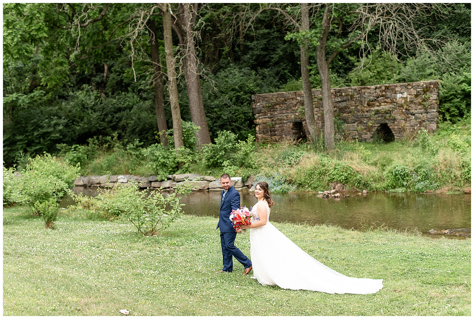 bride and groom walking across open grass area and stone wall