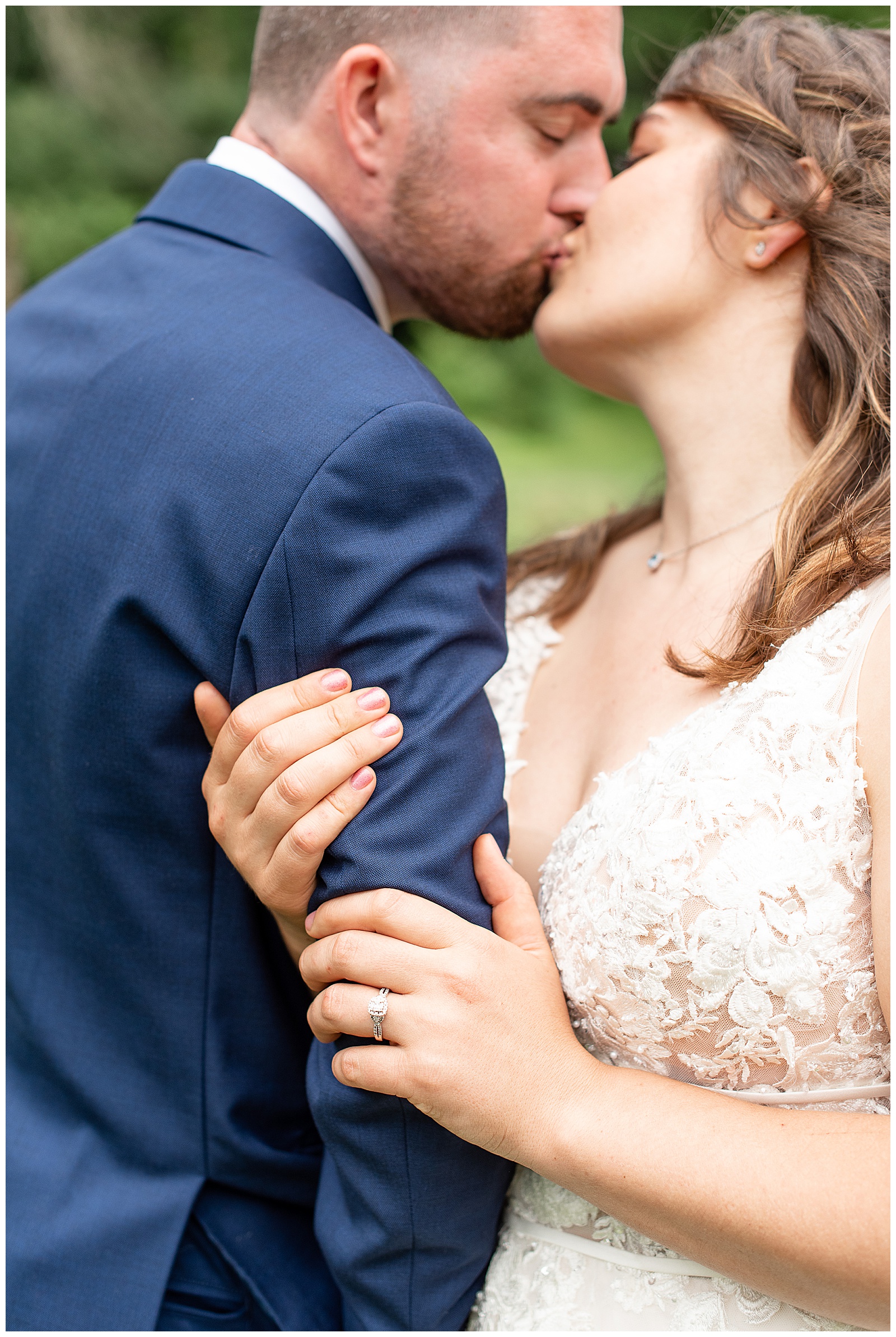 bride and groom kissing while bride holds onto his arm with wedding ring showing