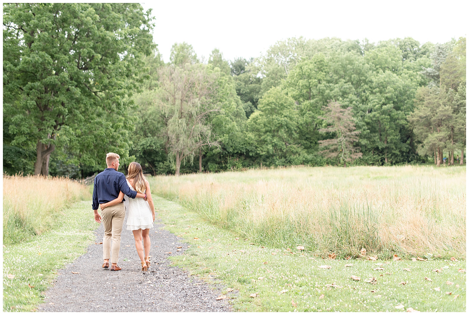 couple walking with arms around each other's backs with wild grass field beside them