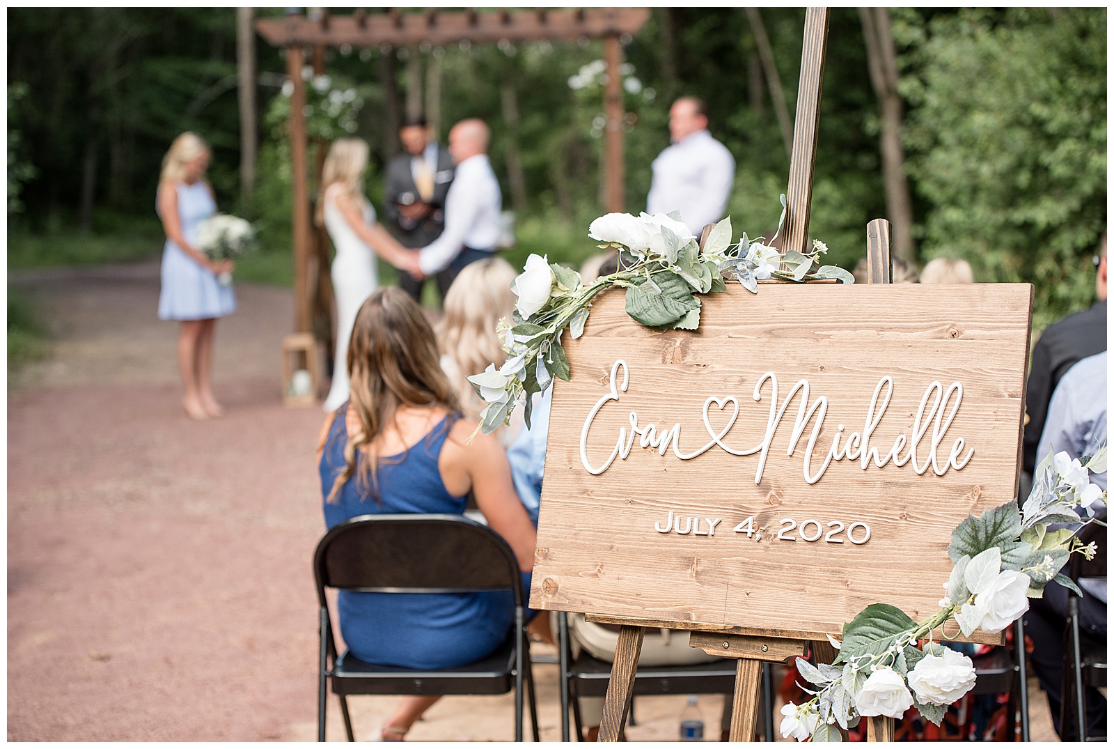 wedding sign at end of aisle with the couple standing up at the alter during the ceremony