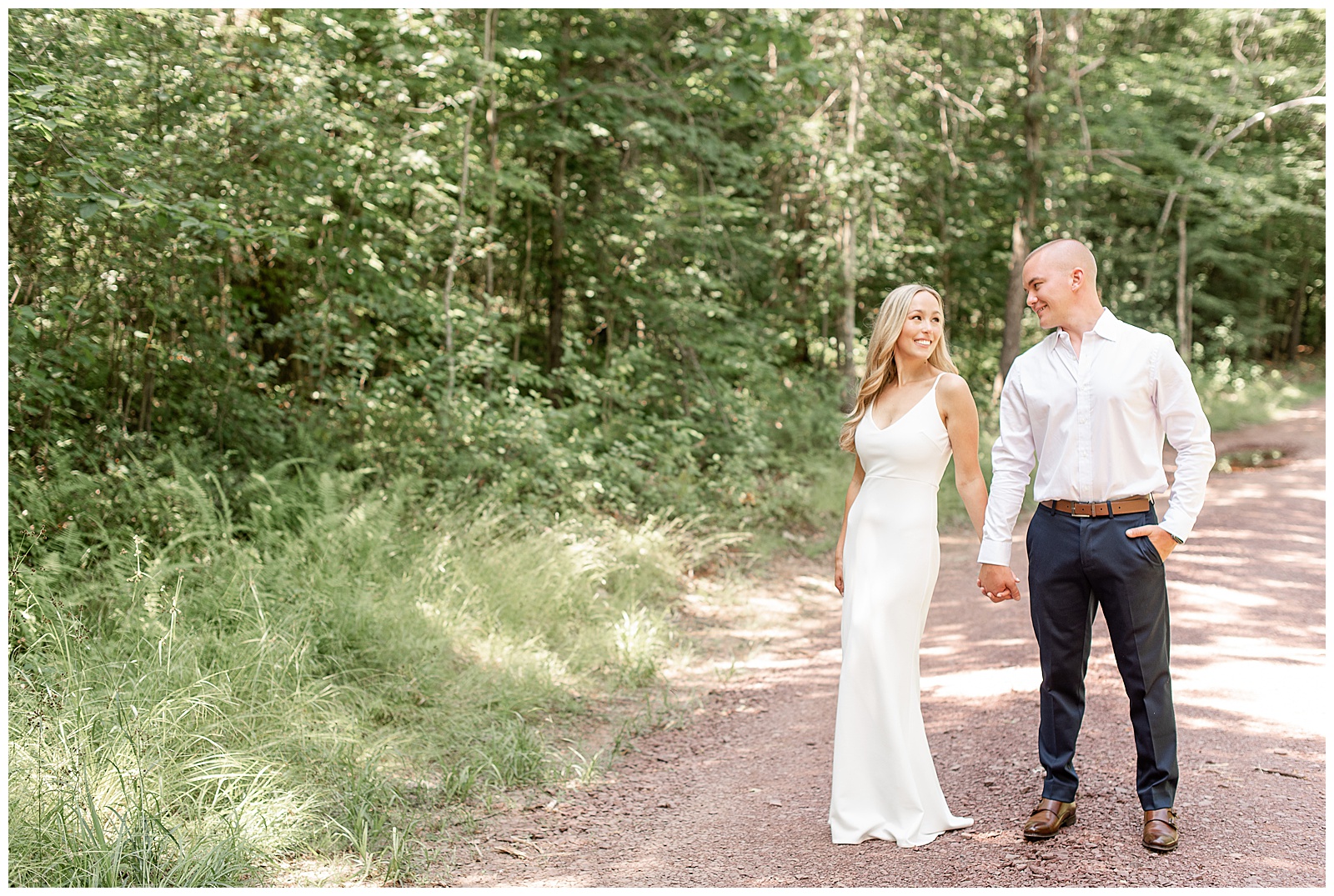 husband and wife holding hands on stone road in middle of woods smiling at each other