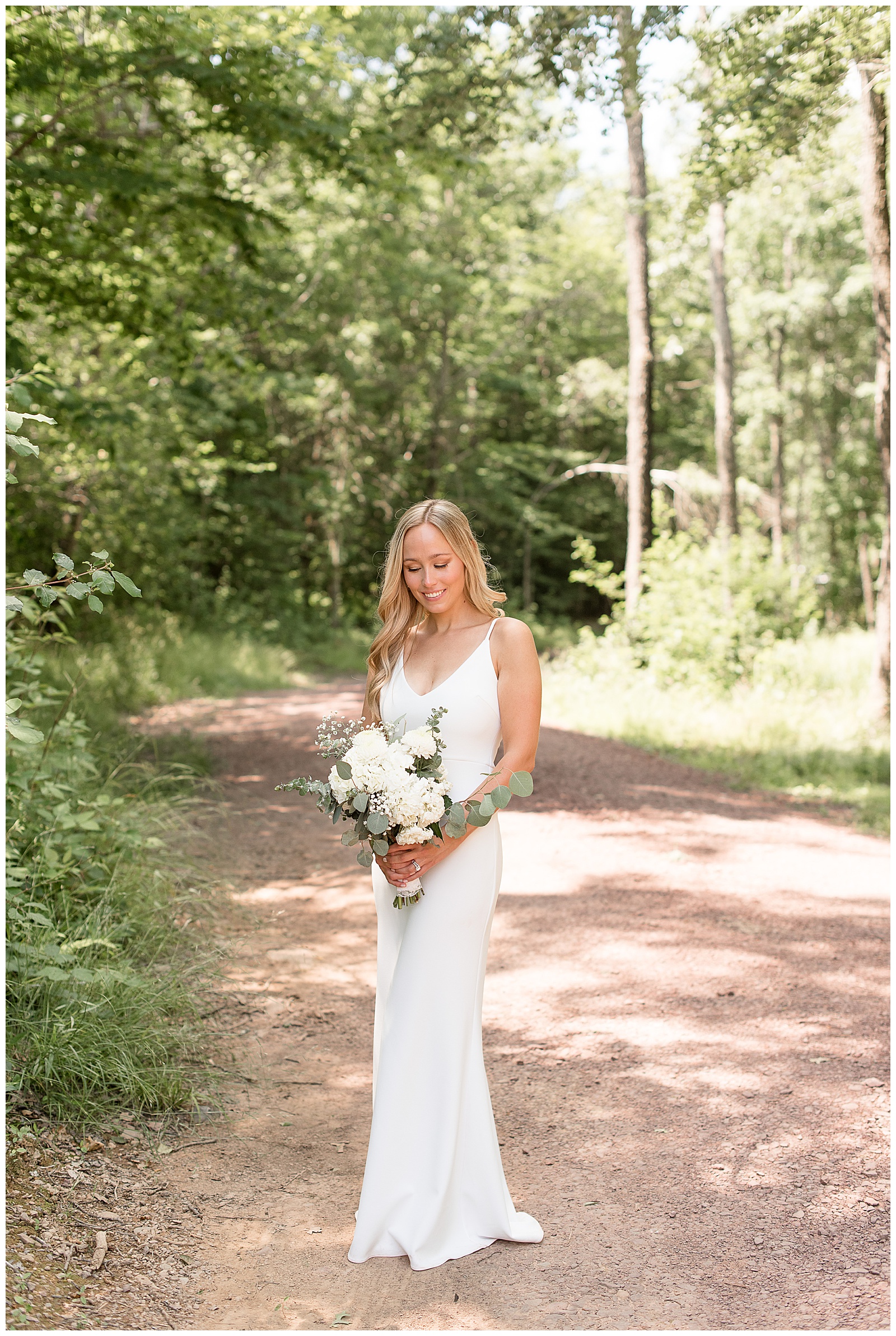 full shot of bride in wedding dress smiling down at white flower bouquet