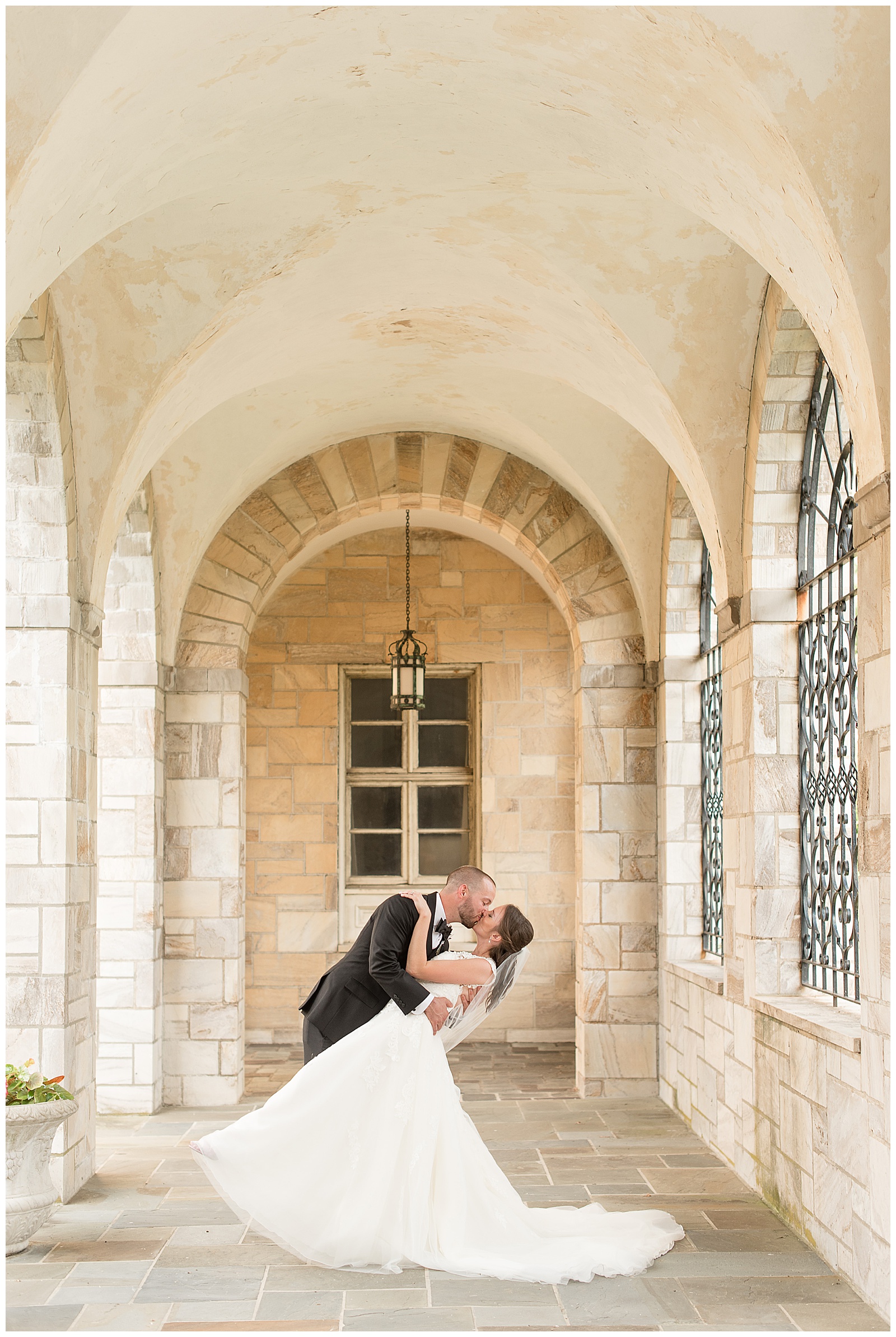 groom dipping bride in hallway between two rows of stone arches