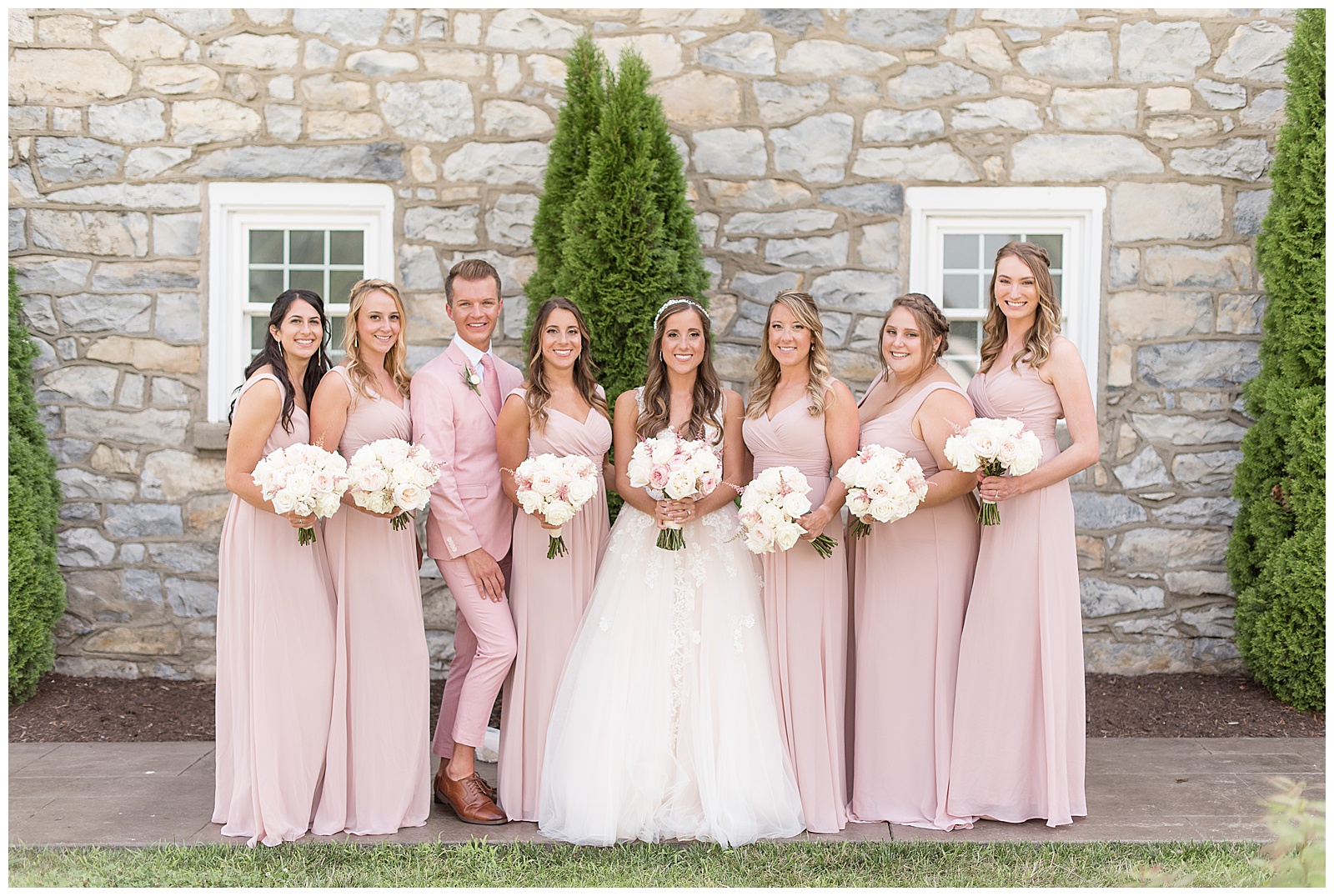 bridesmaids in light pink dresses with one bridesman in a light pink suit smiling beside bride