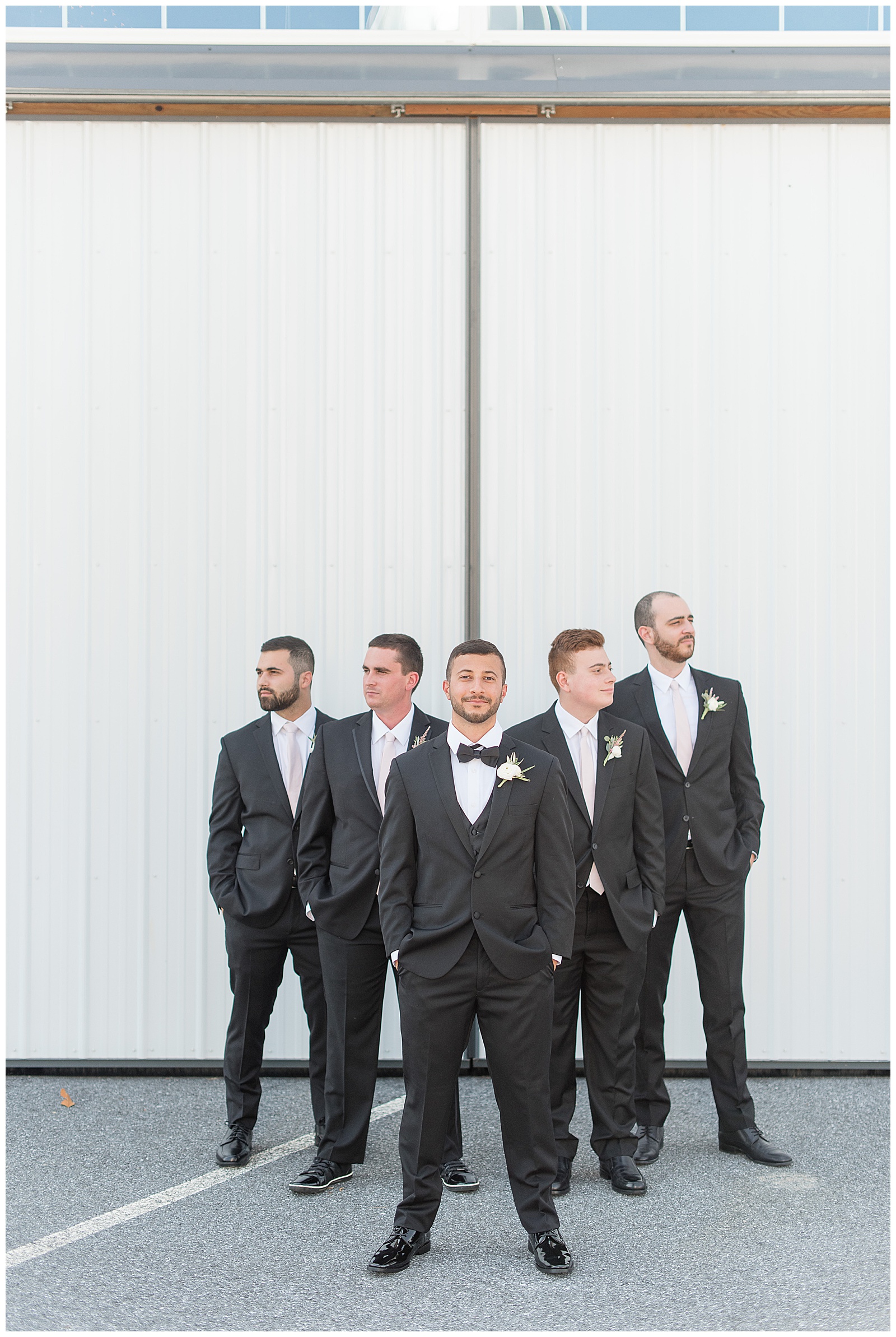 groomsmen looking away from camera as groom looks at camera with serious face, standing in a V formation