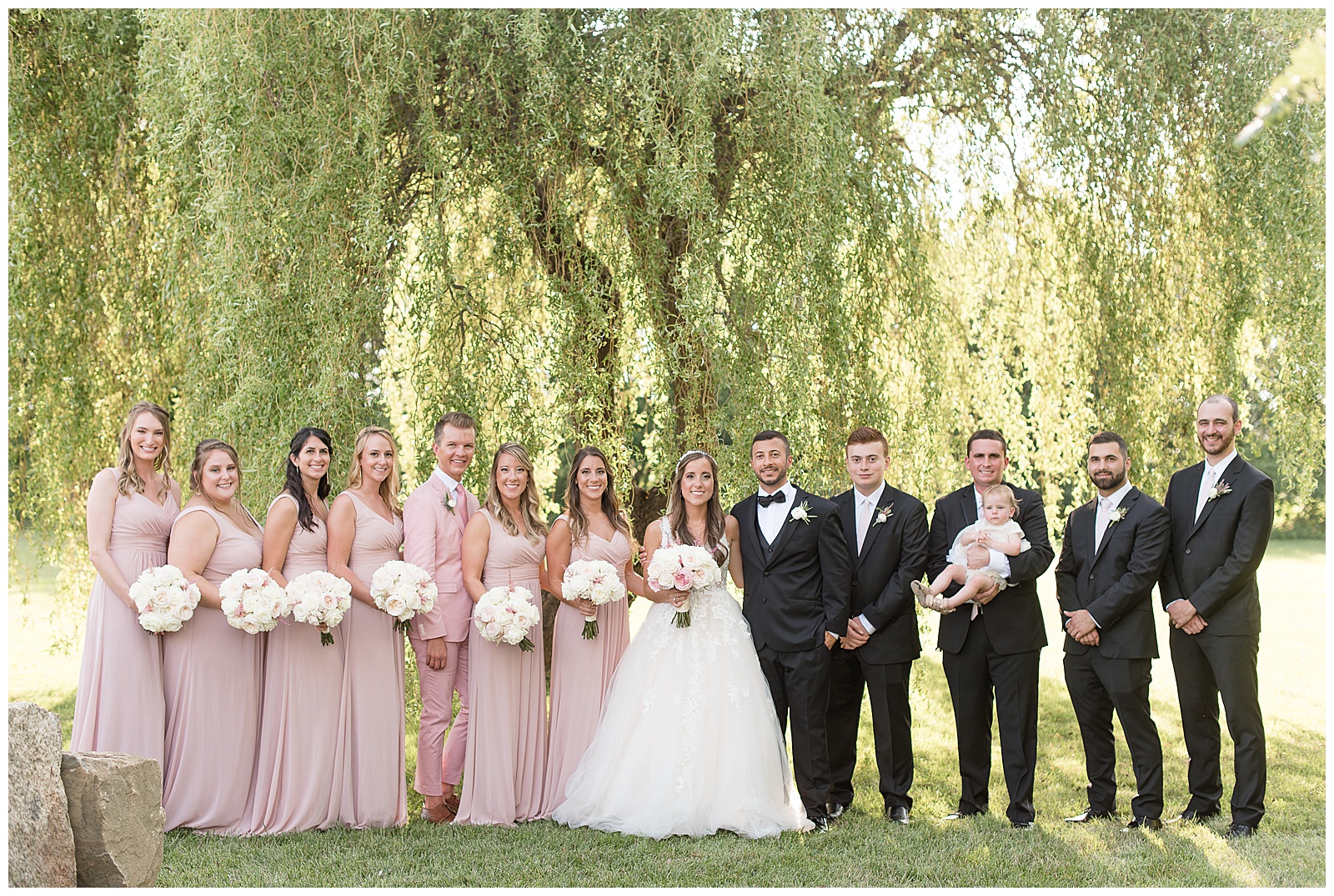 full bridal party smiling to camera standing in front of willow tree