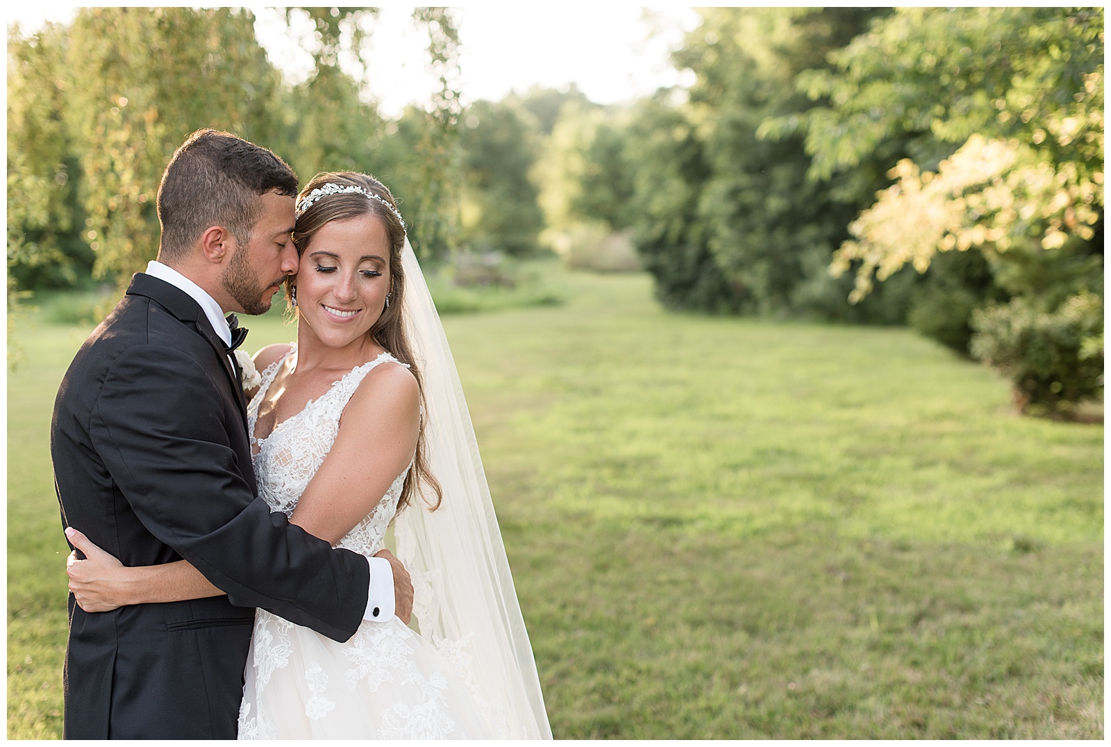 bride and groom with arms wrapped around each other and groom meaning into brides cheek with she smiles down toward her camera