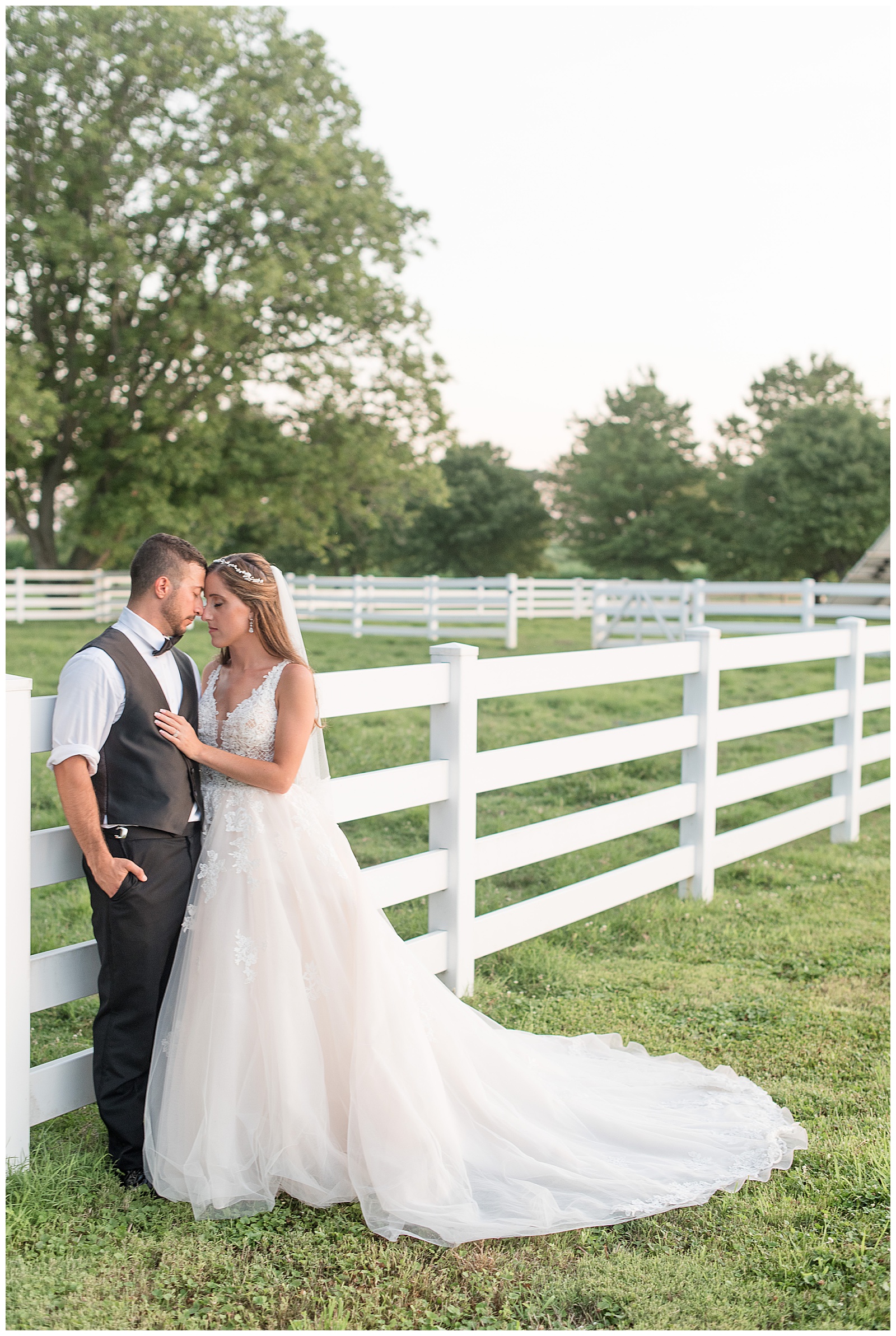 groom leaning against fence while bride leans against him and rests foreheads together