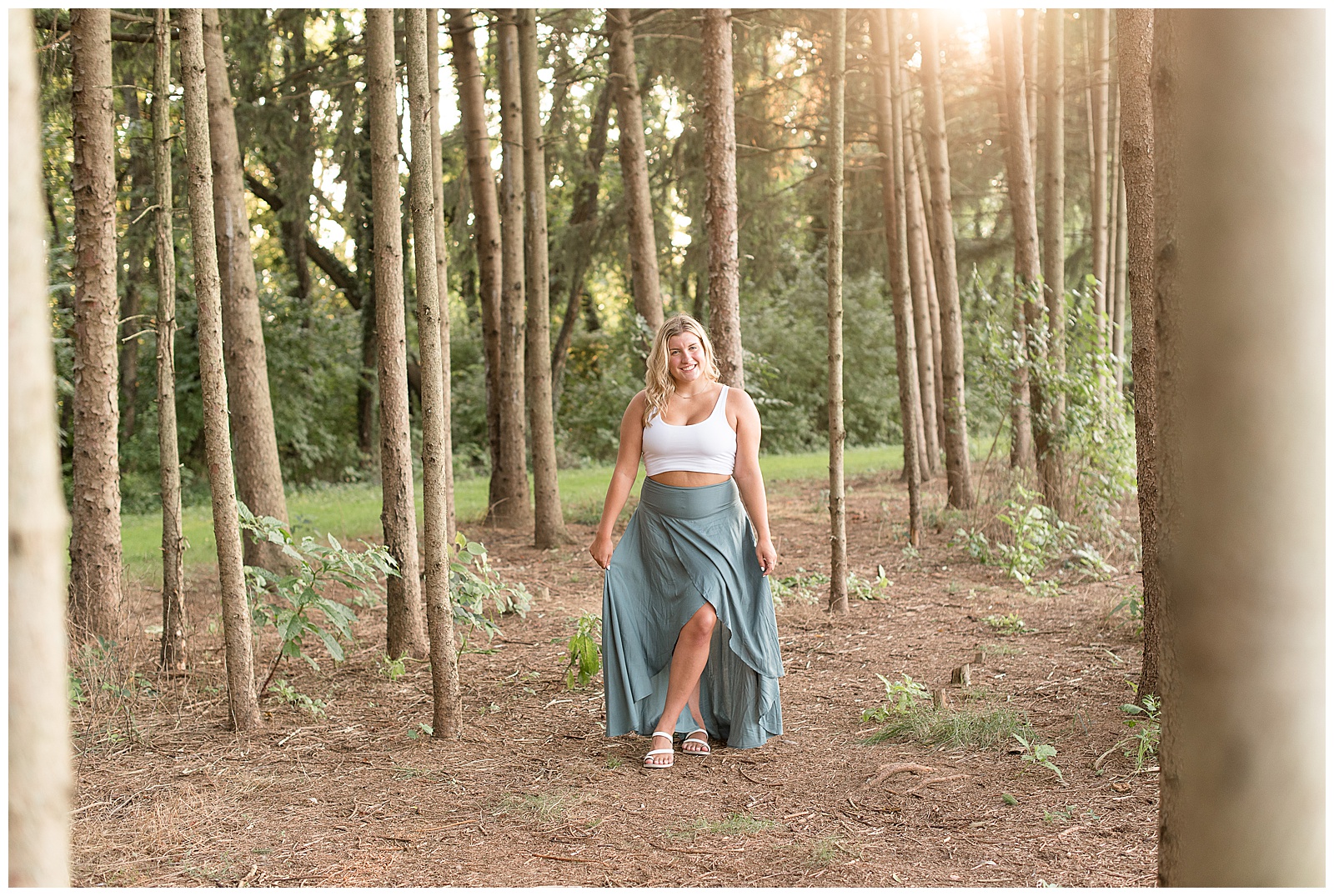 senior walking on path surrounded by pine trees holding skirt with both hands