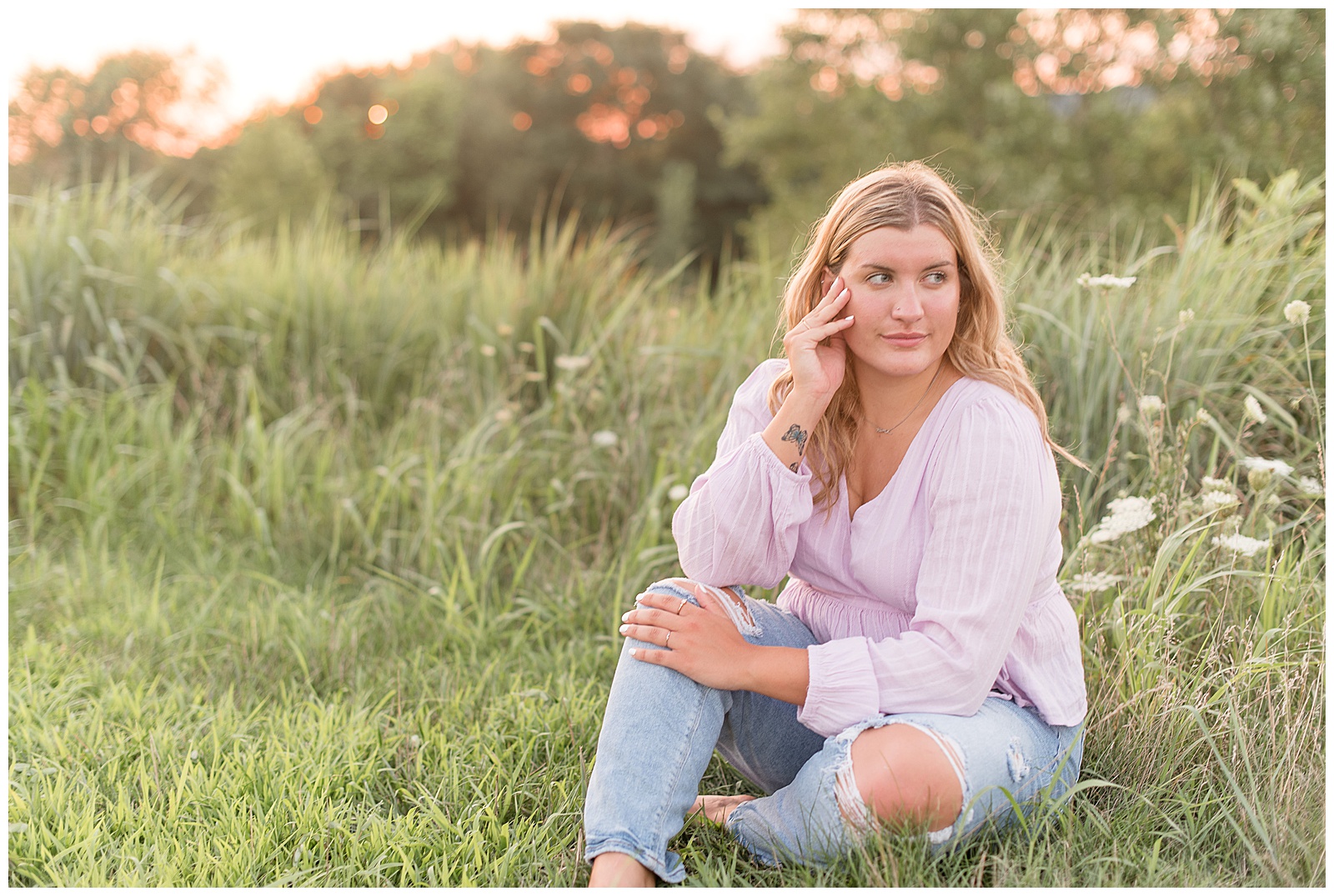 senior sitting in grass area looking off camera with pink sky behind from sun setting