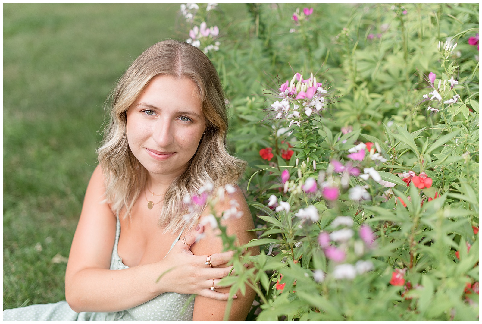 senior sitting beside colorful flowers looking at camera with hand resting on shoulder