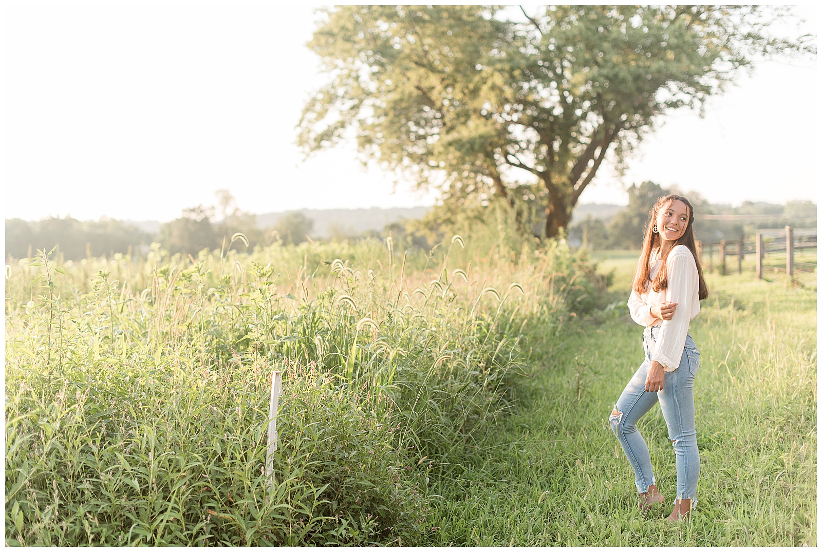 senior holding arm and smiling off side of camera in path between tall grasses on farm in Elizabethtown