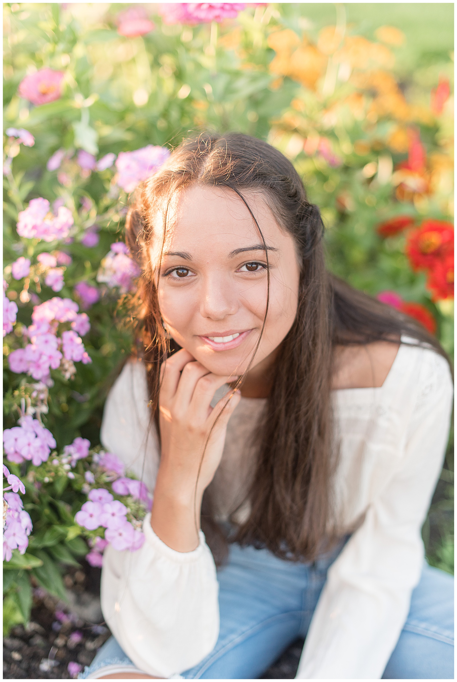 senior leaning forward and resting chin on hand while smiling at camera with florals around