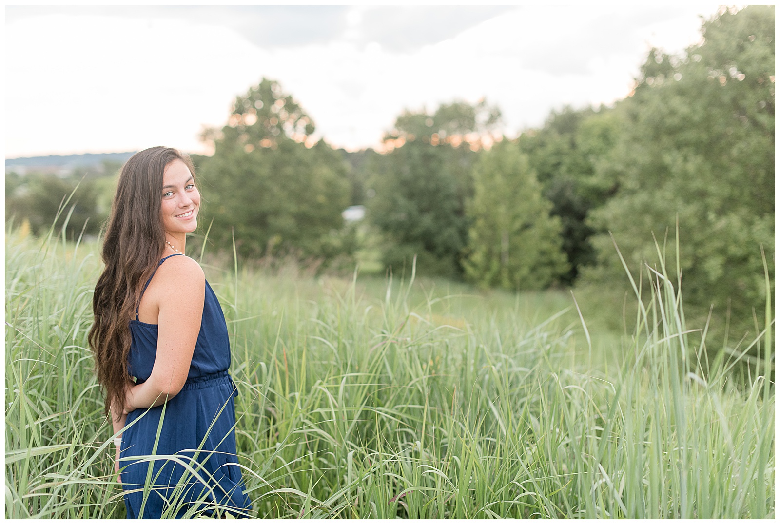 senior girl looking over shoulder in blue romper with tall grasses around