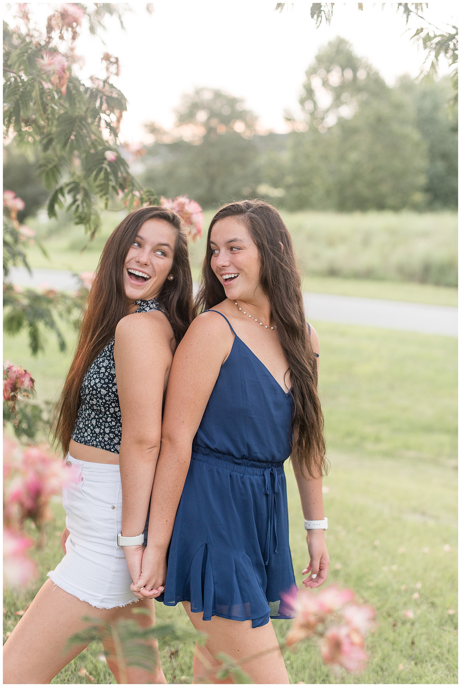 twin senior session at Overlook Park, with seniors holding hands and backs against each other smiling at each other over shoulders