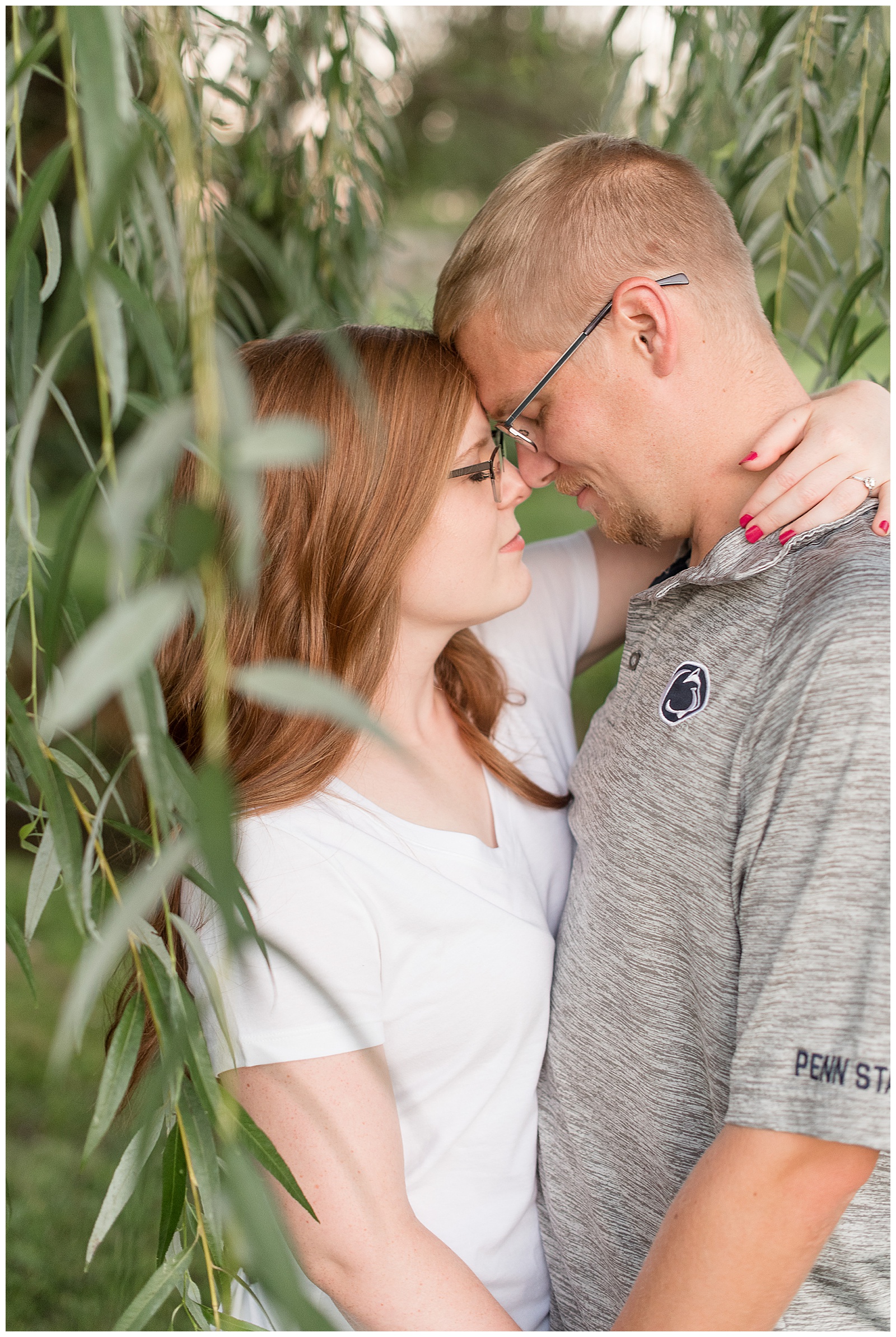 couple standing among willow trees facing each other with arms wrapped around and foreheads touching
