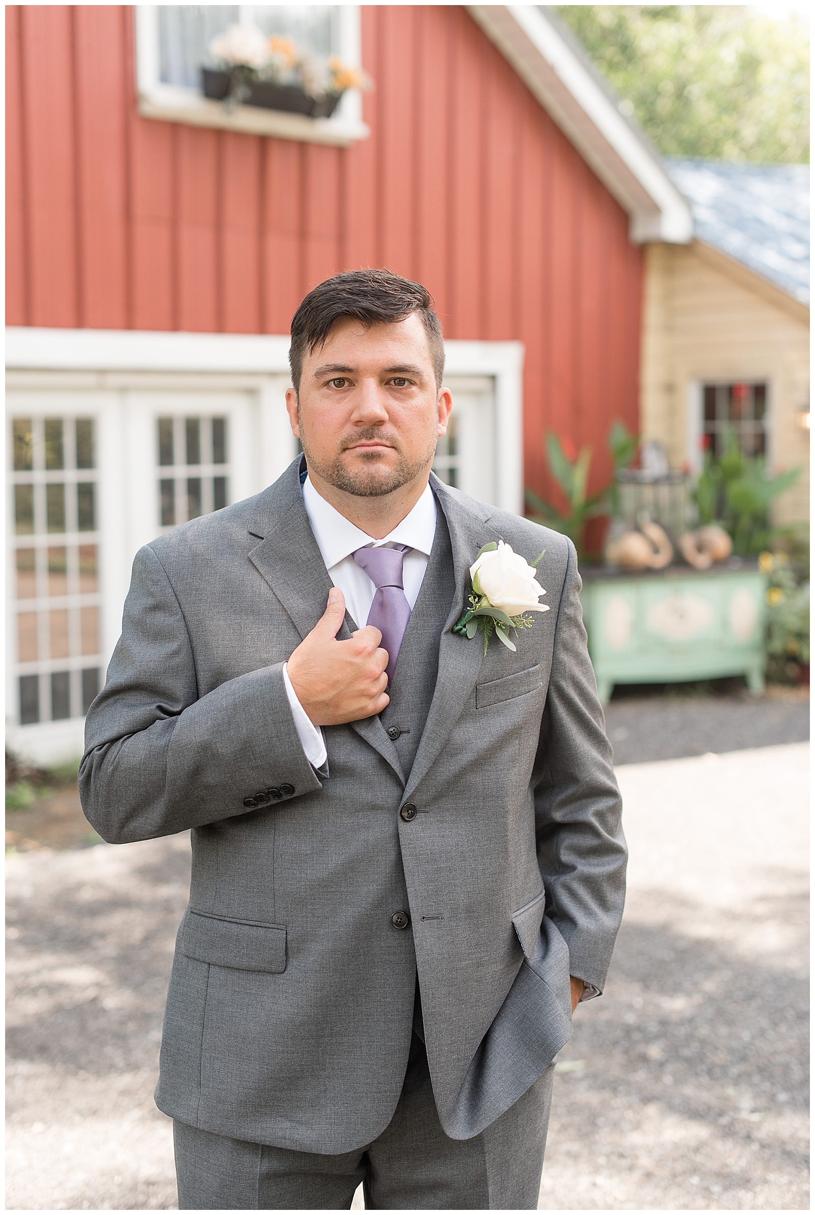 groom looking at camera standing in front of red barn