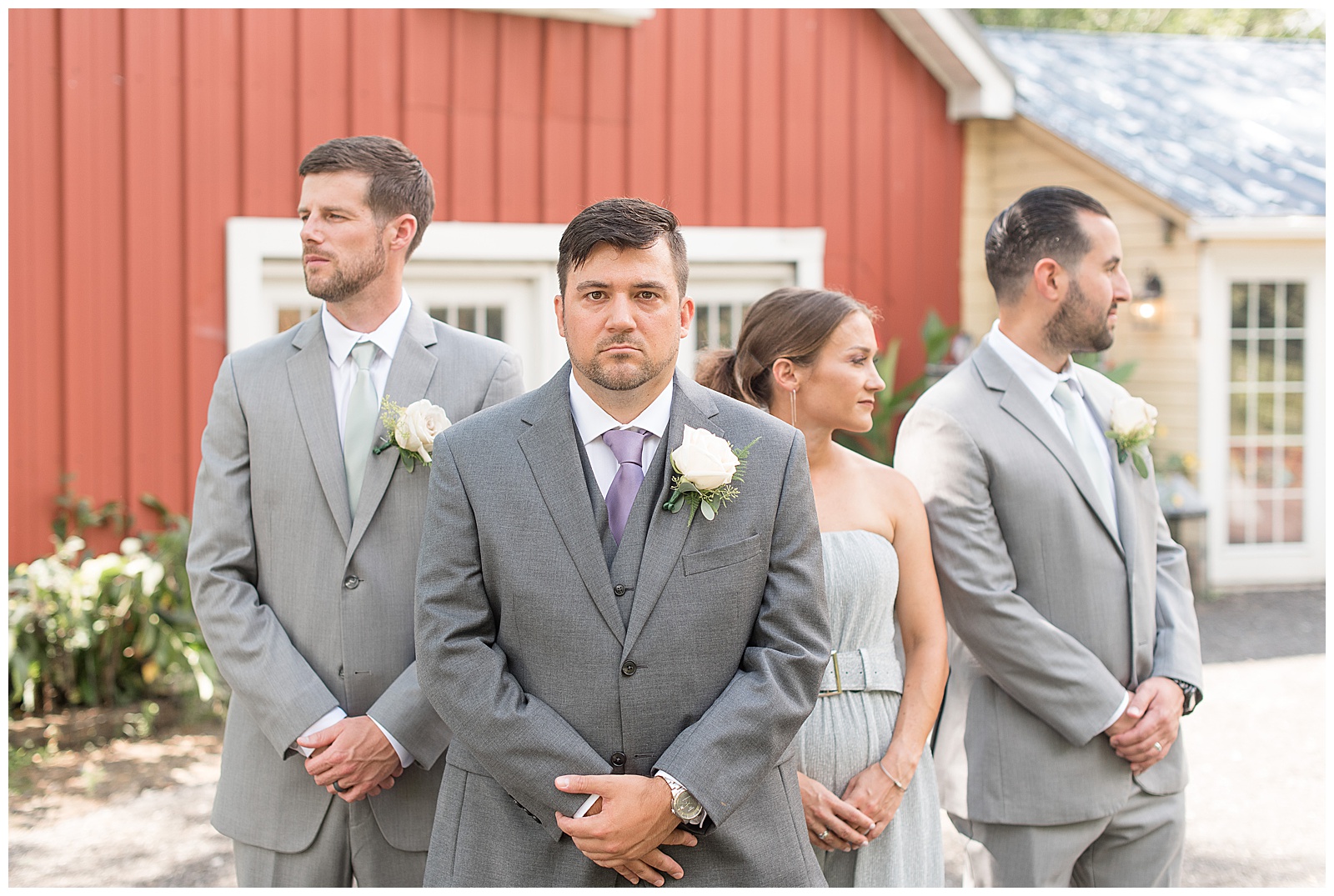groom looking at camera while groomsmen look away from camera with red barn behind at Fallen Tree Farm