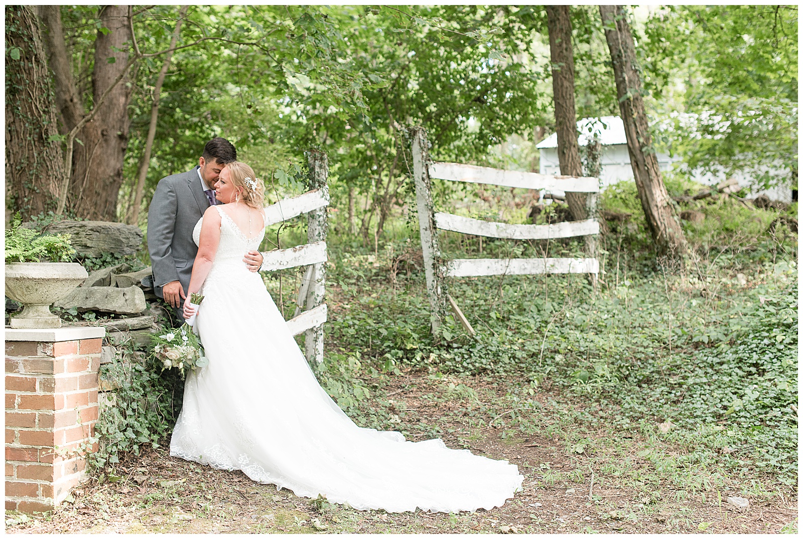 groom leaning on stone ruins at Fallen Tree Farm with bride leaning up against him and flower bouquet down to side