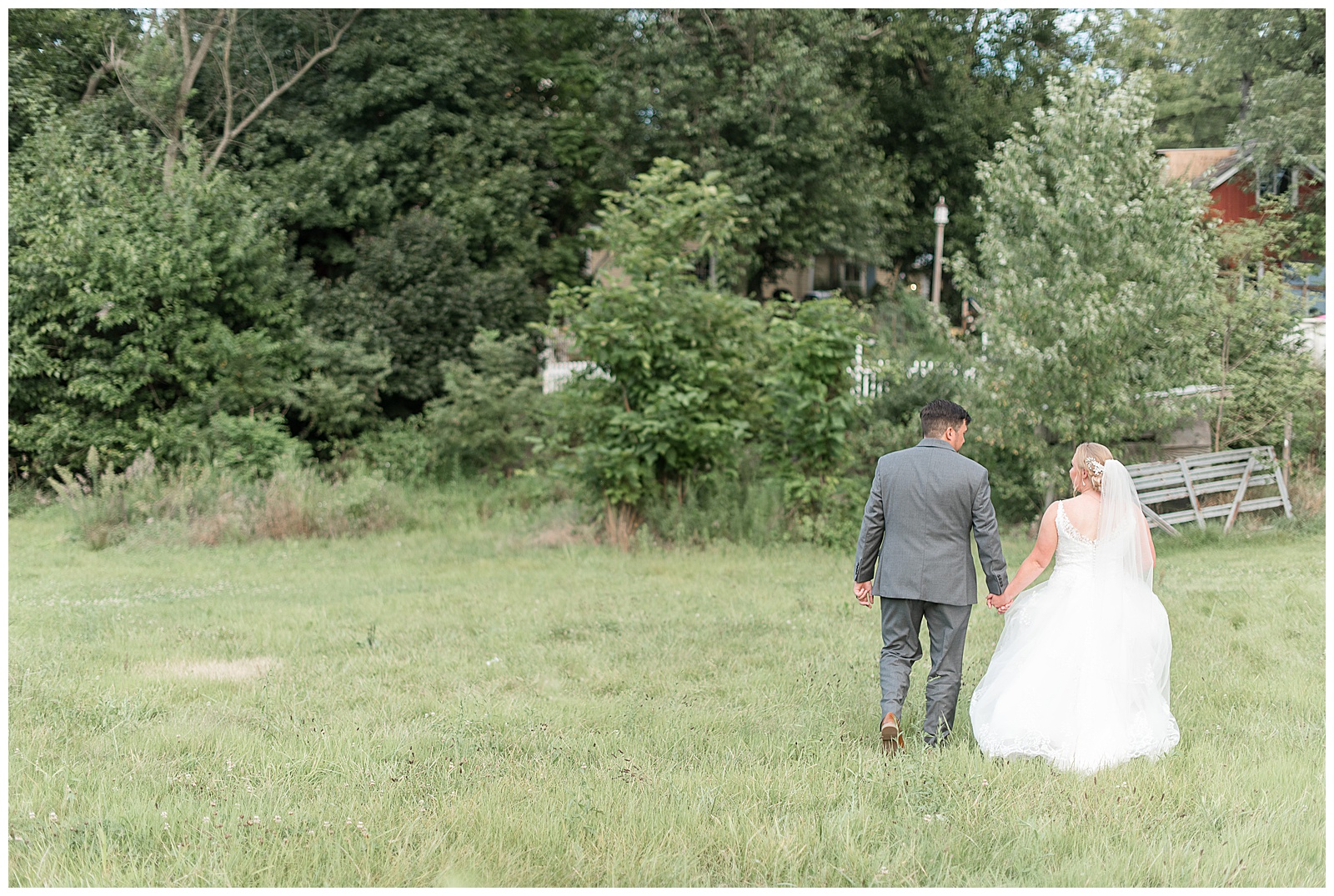 husband and wife walking away from camera smiling at each other through open field of tall grasses at Fallen Tree Farms Bed and Breakfast