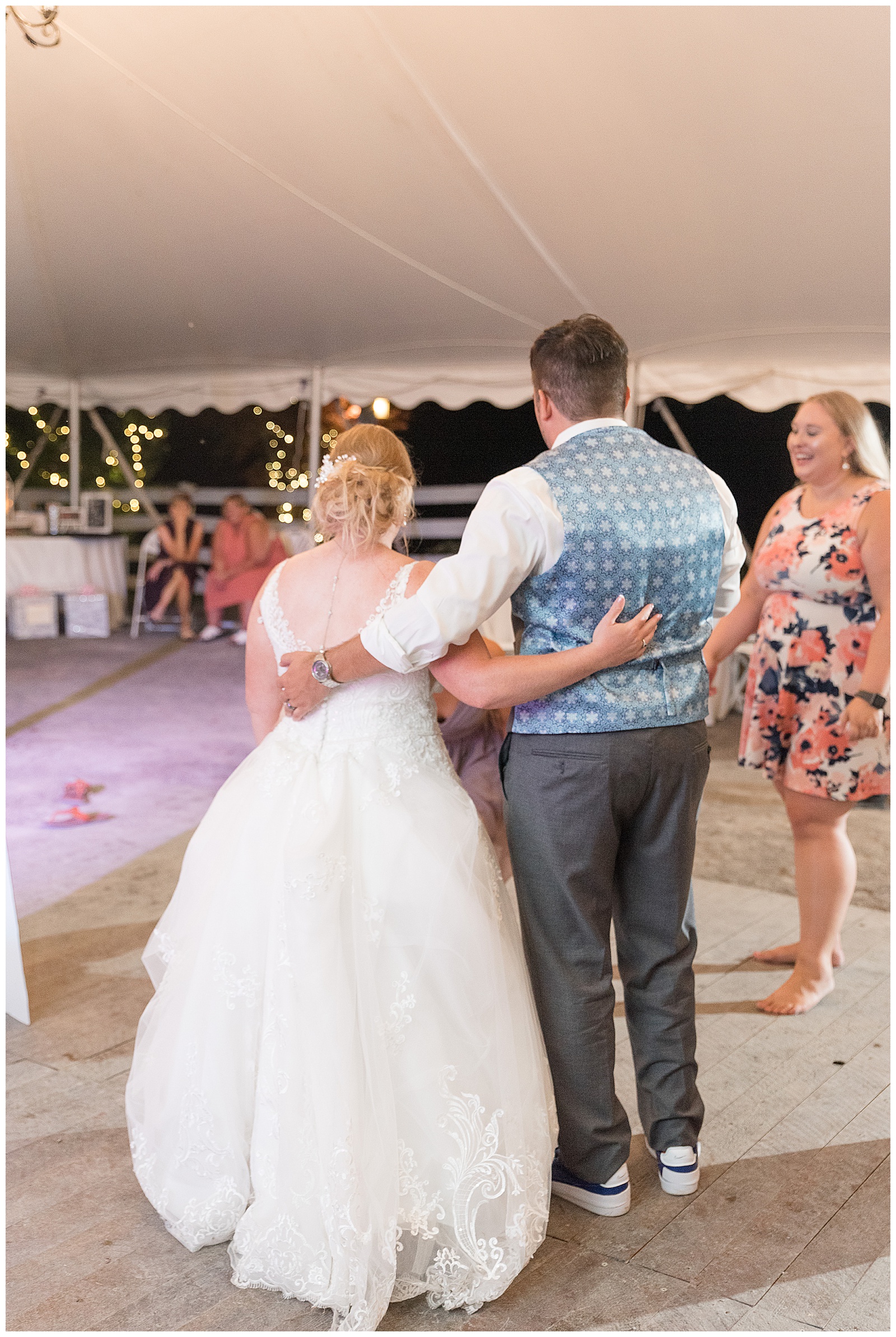 bride and groom standing on dance floor with arms wrapped around each other watching guests dance