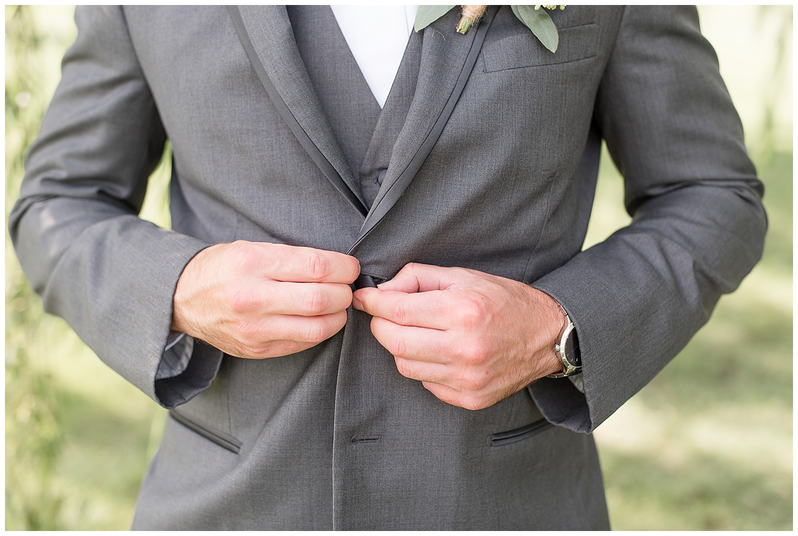 really close up photo of the groom in his dark gray suit buttoning up the top button on his suit coat with his watch showing on his left wrist while at Lakefield Weddings venue in Manheim, PA