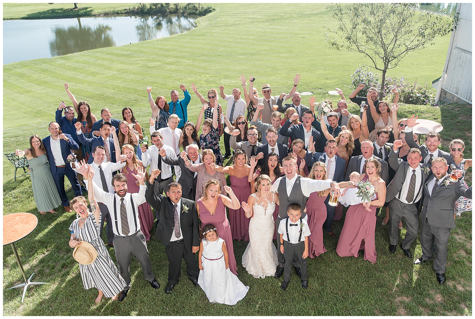 group shot of wedding couple, their bridal party, and guests outdoors in grass field with pond in the background on sunny day at Lakefield Weddings in Manheim, PA