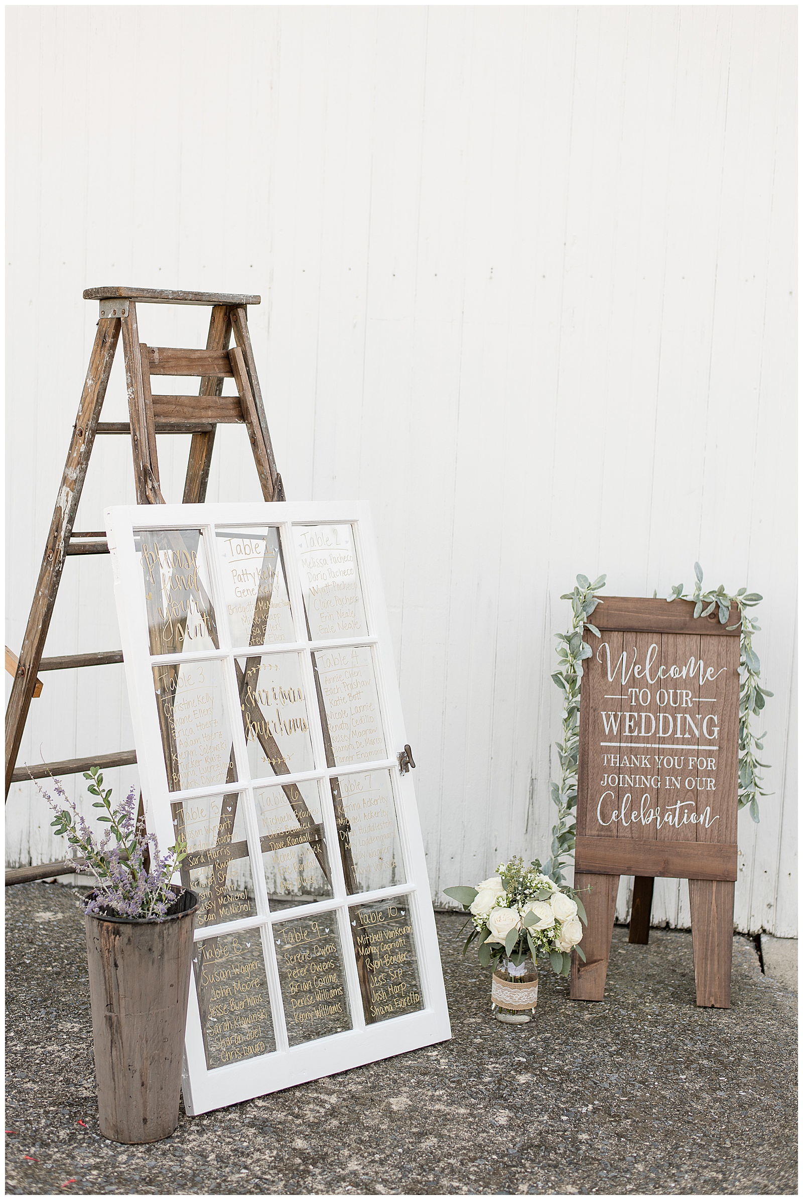 photo of their welcome display with white window frame guest list propped against brown wooden ladder with potted plants arranged around it and wooden welcome sign from wedding ceremony on right side in front of white barn at Lakefield Weddings in Manheim, PA